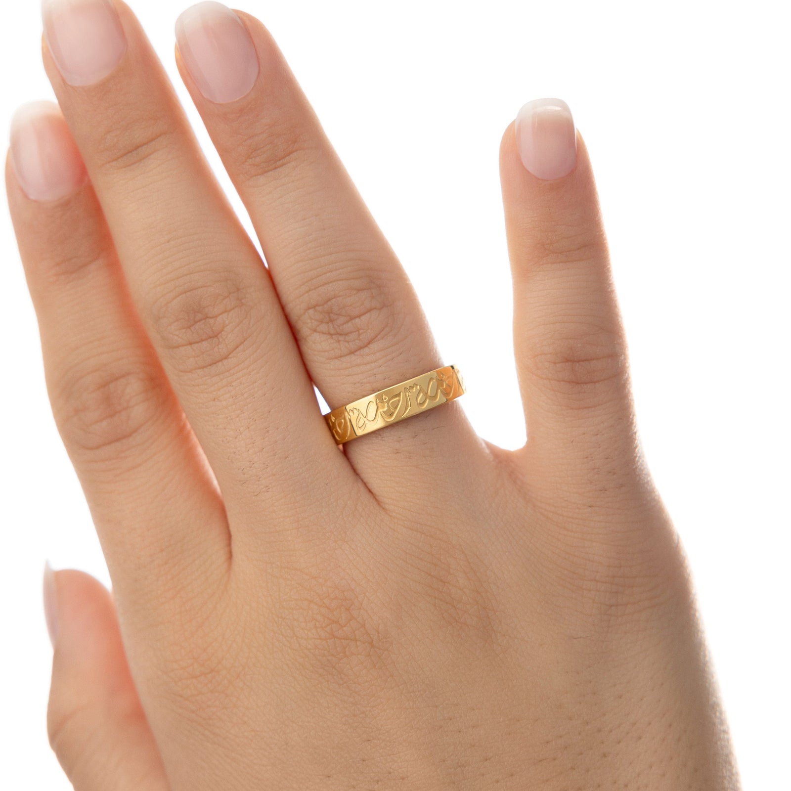 Woman’s hand facing outward wearing the gold Rahma Mercy Ring on the ring finger, Arabic calligraphy wrapping around the band.