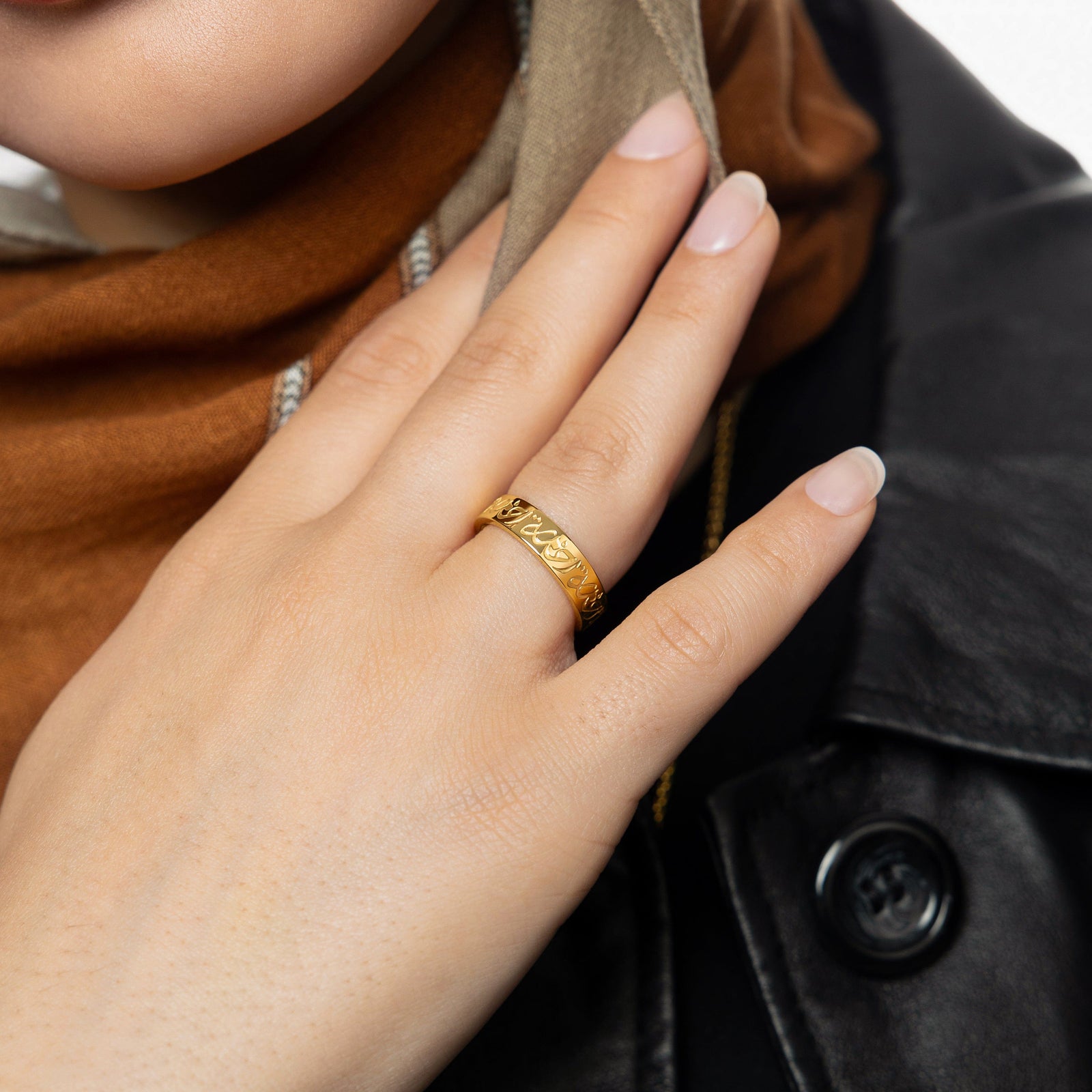 Woman wearing the gold Rahma Mercy Ring, styled with a neutral-toned hijab and black leather jacket, hand resting on her collar.