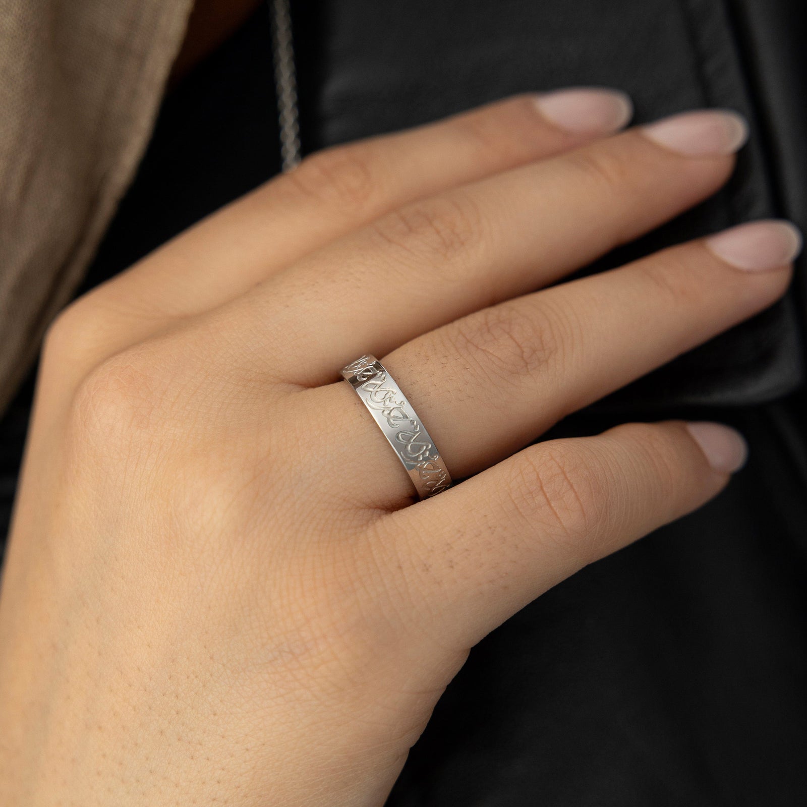 Woman wearing the silver Rahma Mercy Ring, hand placed near her chest over a black top, Arabic engraving visible.