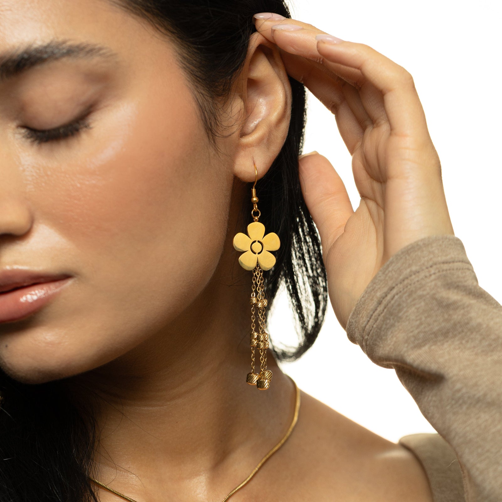 Woman wearing the gold Raining Flower Earrings, lightly touching her hair, with the dangling floral design visible against her skin.