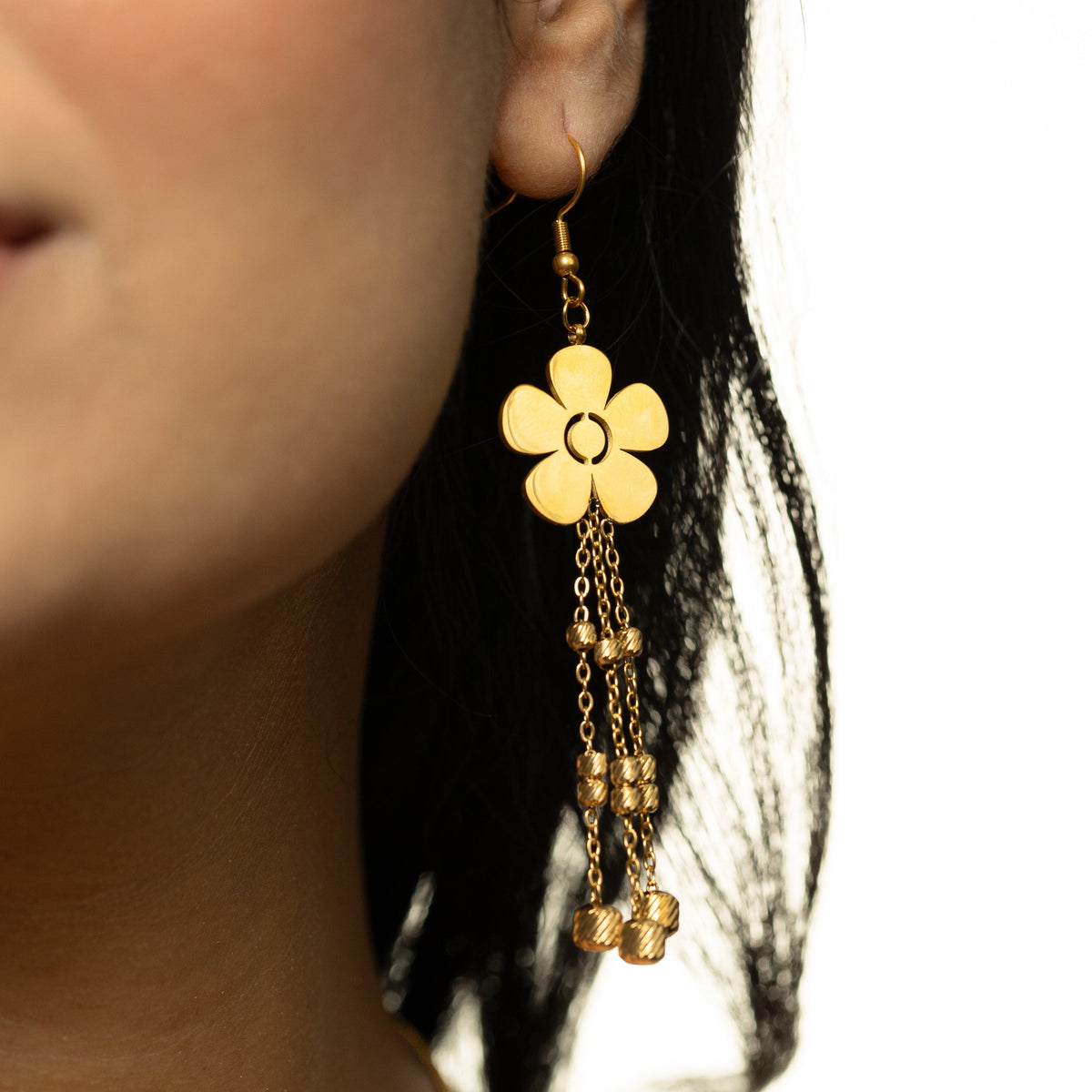 Close-up of a single gold Raining Flower Earring worn on the ear, showing the dangling beaded chains swaying below the flower.