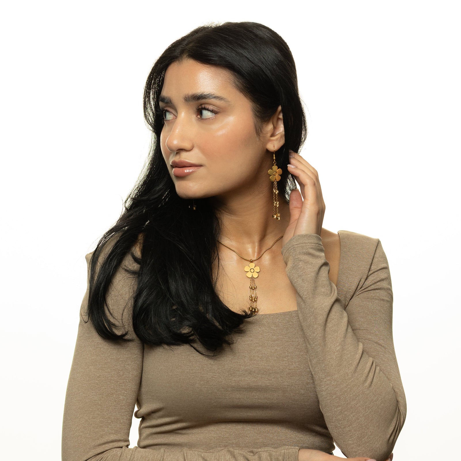 Woman wearing the full gold Raining Flower Earrings and matching necklace with flower pendant, styled with a beige square-neck top.