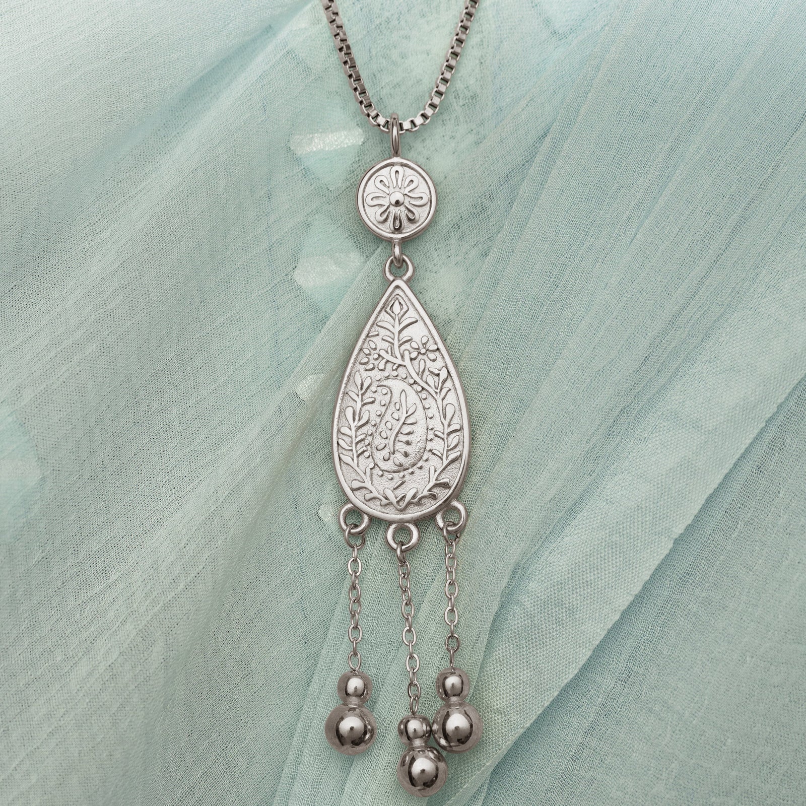 Close up photo of the silver pendant on a light blue fabric background.