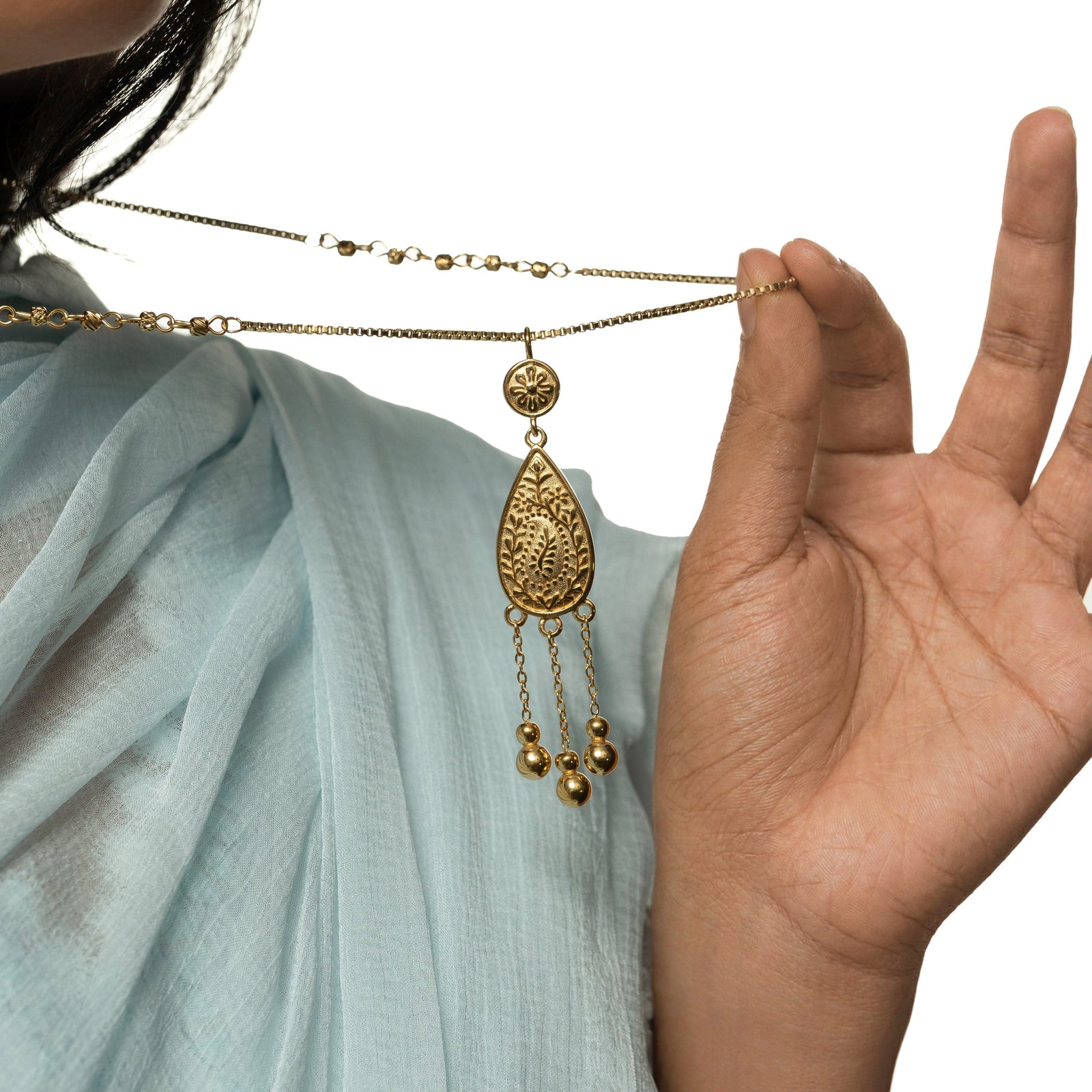 Model pulls the thin gold box chain to show the details of the pendant design of the gold Raining Paisley Necklace.