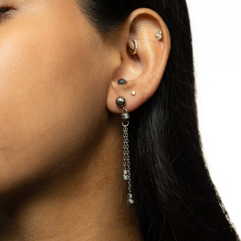 Woman wearing a single silver earring with double chain dangles ending in ribbed bead charms.