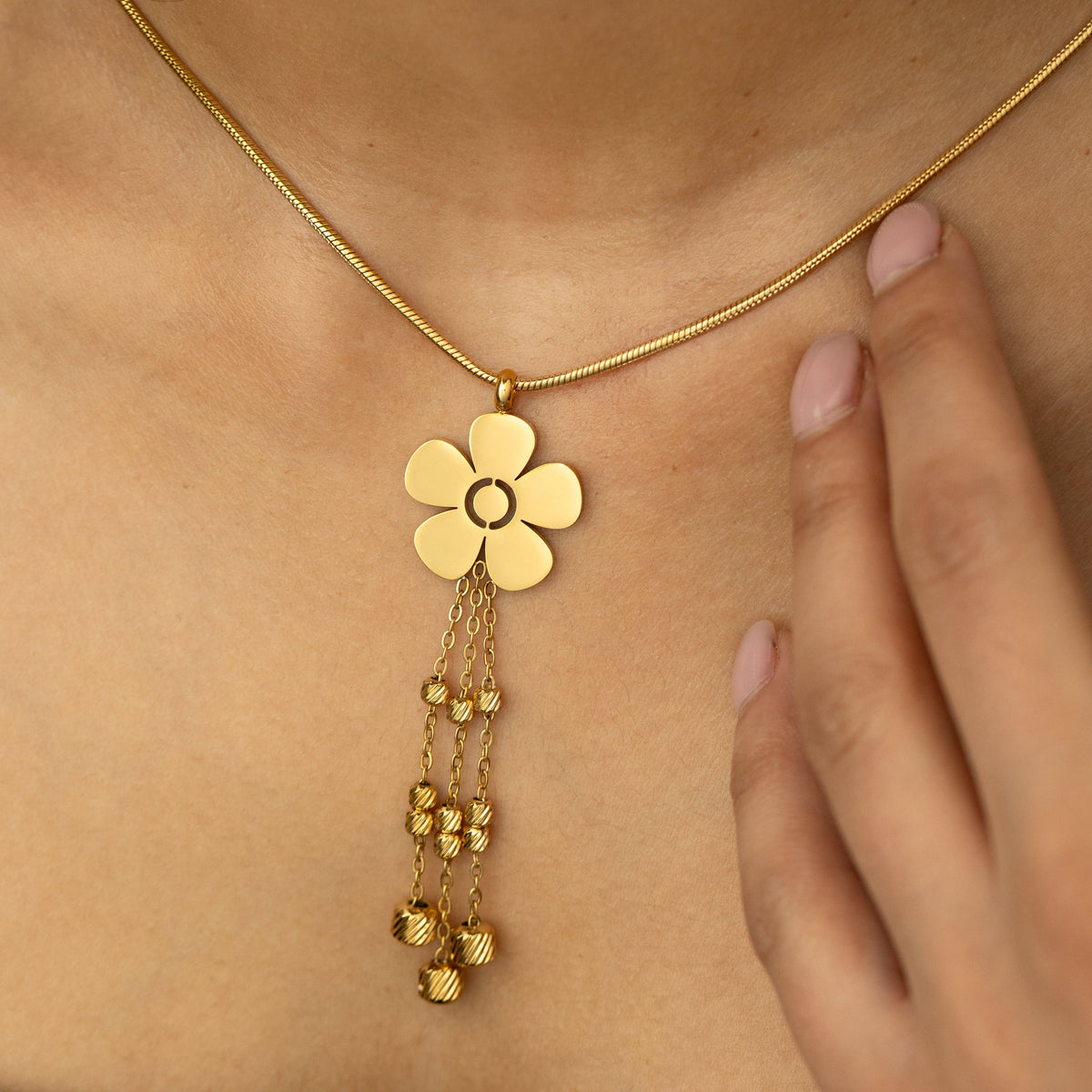 Close-up of the gold Raining Flower Necklace worn on the neck, showing the flower pendant with bead-detailed chains resting against the skin.