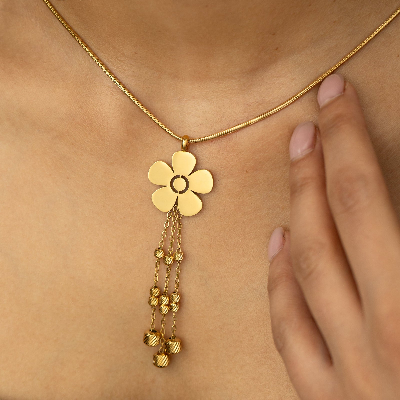 Close-up of the gold Raining Flower Necklace worn on the neck, showing the flower pendant with bead-detailed chains resting against the skin.