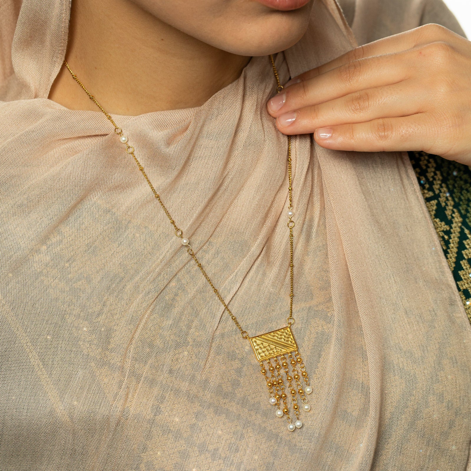 Close up photo of the gold Raining Pearls Keffiyeh necklace and model touching the thin gold chain.