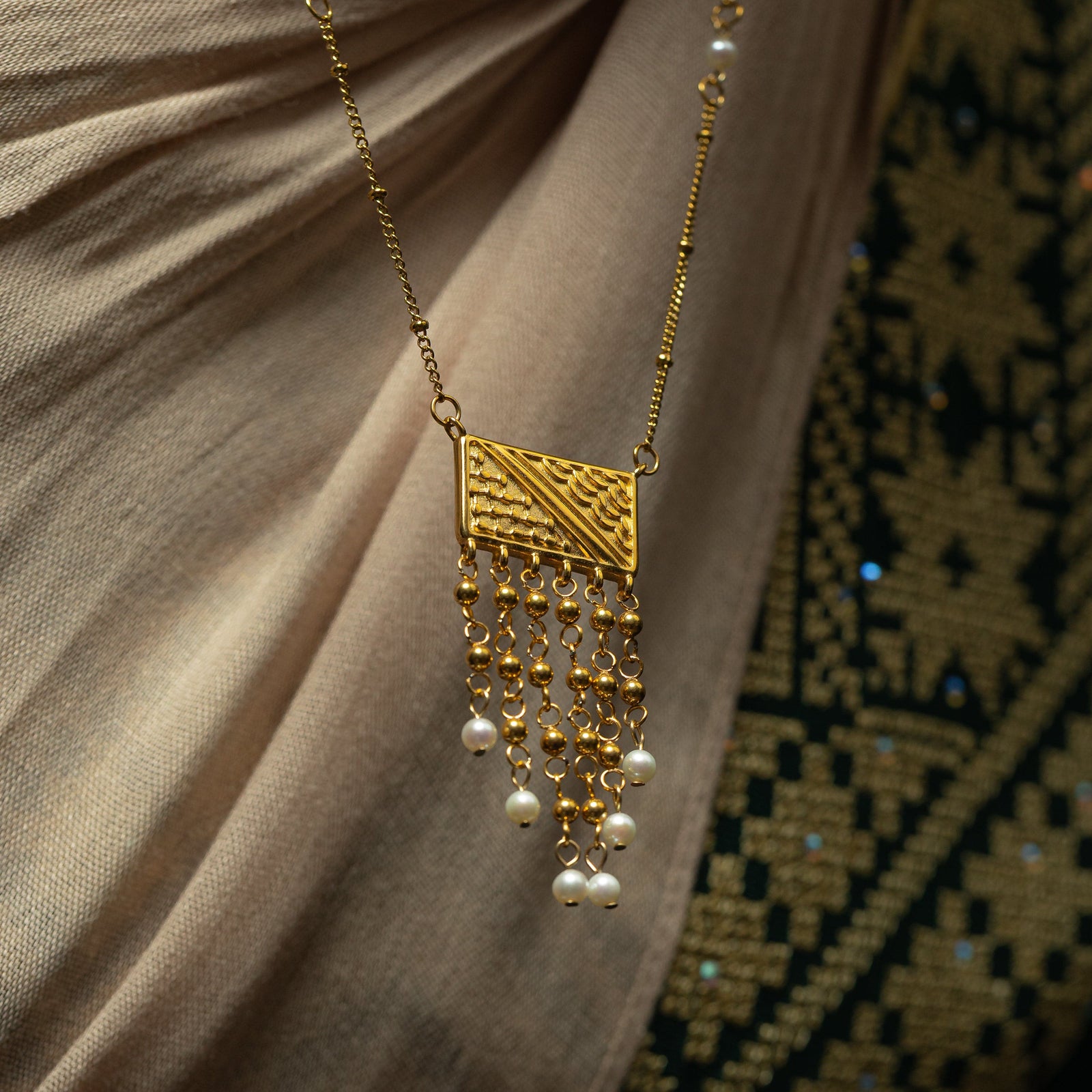 Close up photo of the pendant of the gold Raining Pearls Keffiyeh necklace hanging from it's thin gold chain finished with pearl orbs.