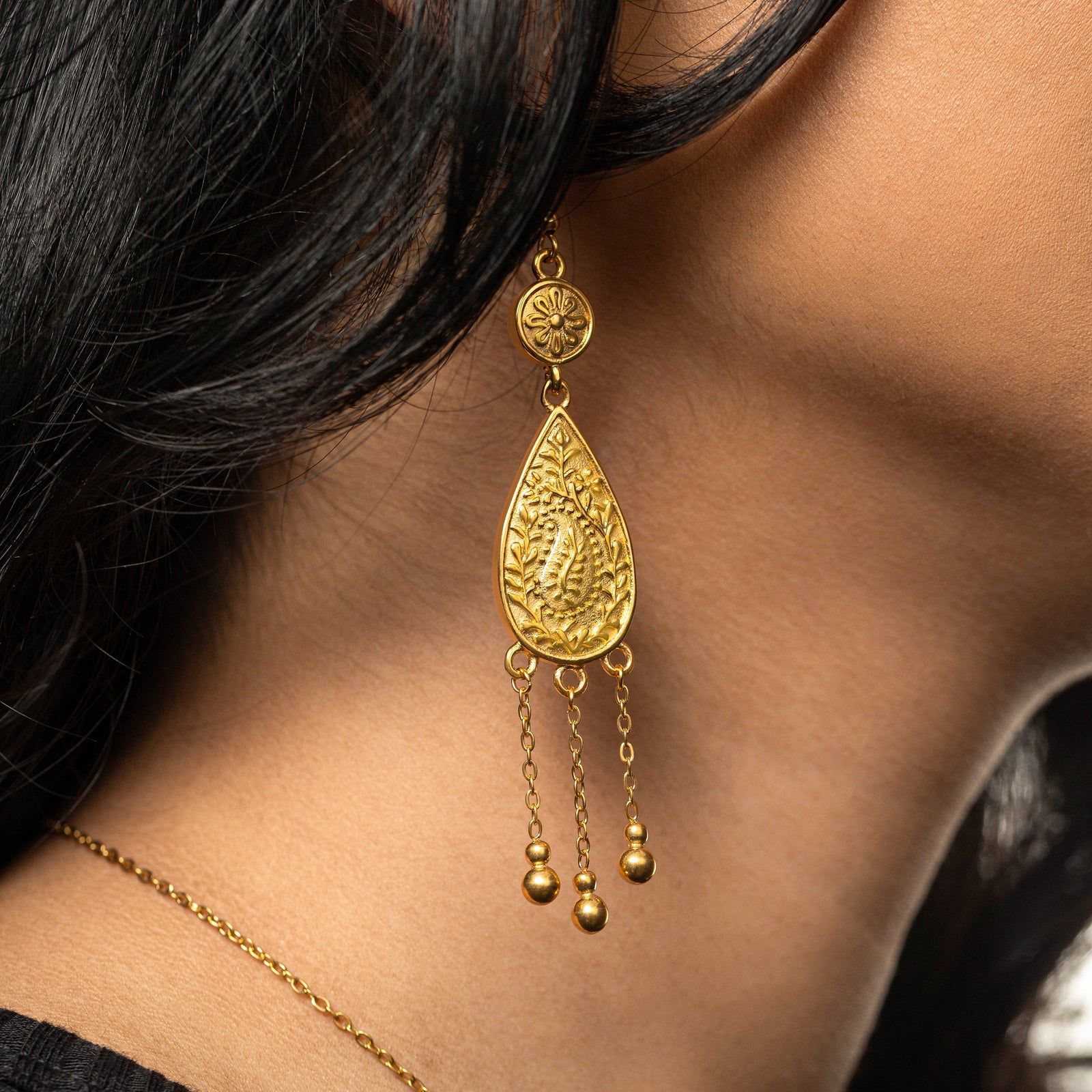 Woman wearing one Raining Paisley Earring, showing the gold teardrop pendant with a paisley pattern and three dangling chains.