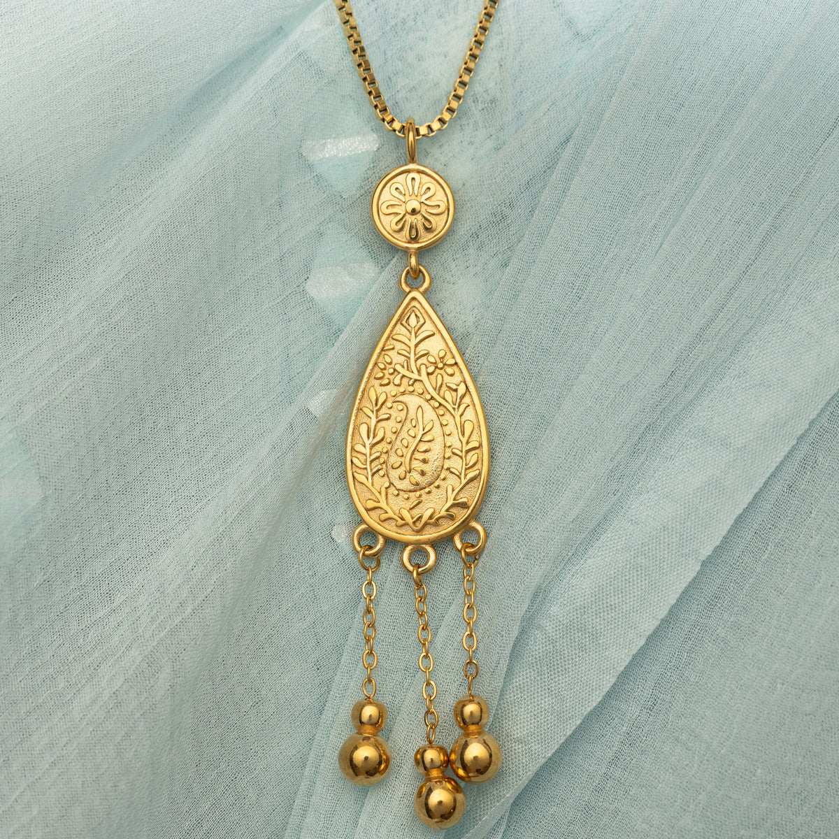 Close up photo of the gold pendant on a light blue fabric background.