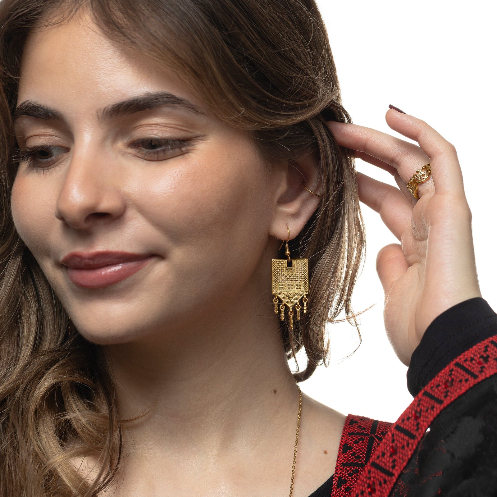 Photo of the model looking away from the camera, holding their hair away from their left ear. The model is wearing the gold Raining Tatreez Earrings