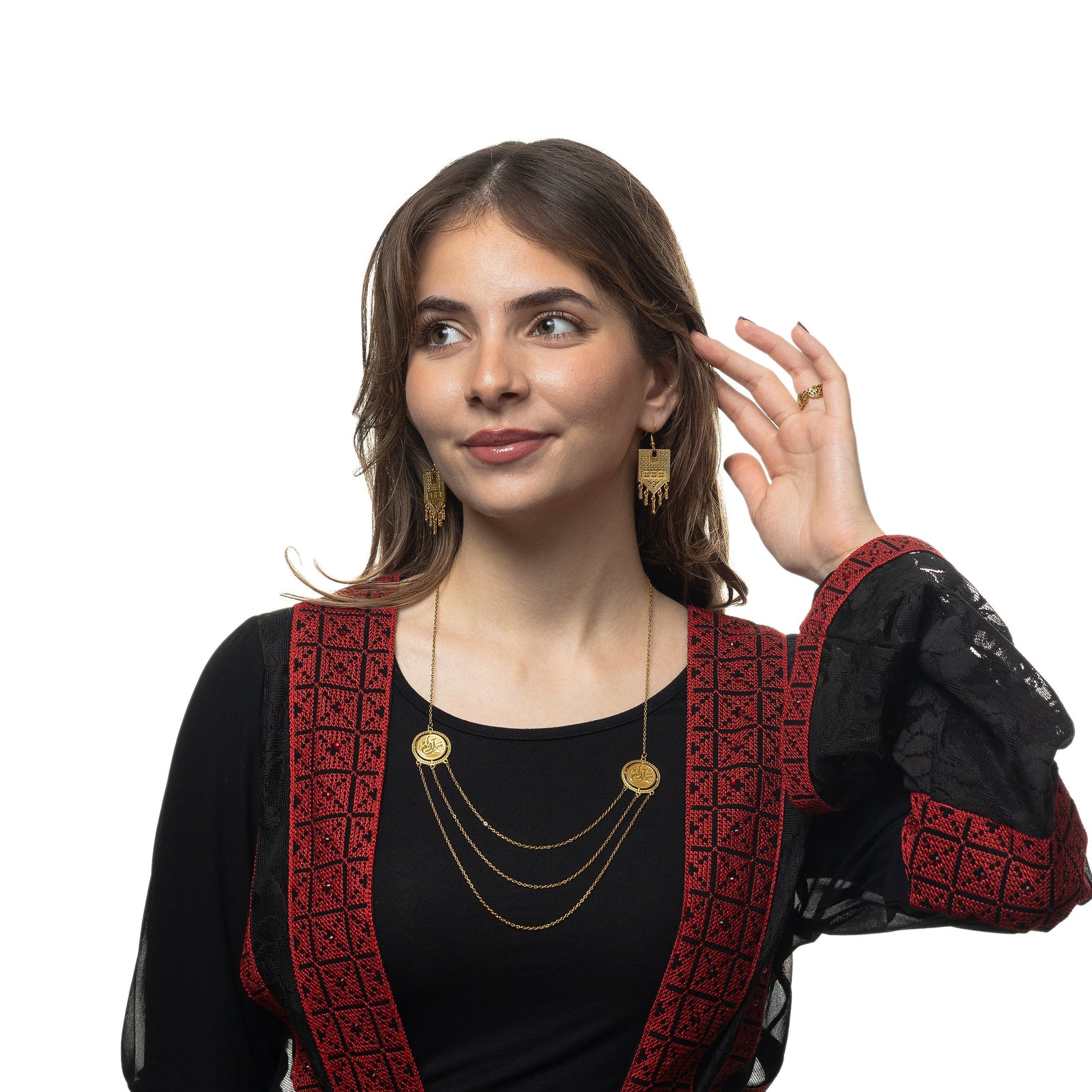 Photo of the model looking away from the camera, holding their hair away from their left ear. The model is wearing the gold Raining Tatreez Earrings, gold necklace, and gold ring.