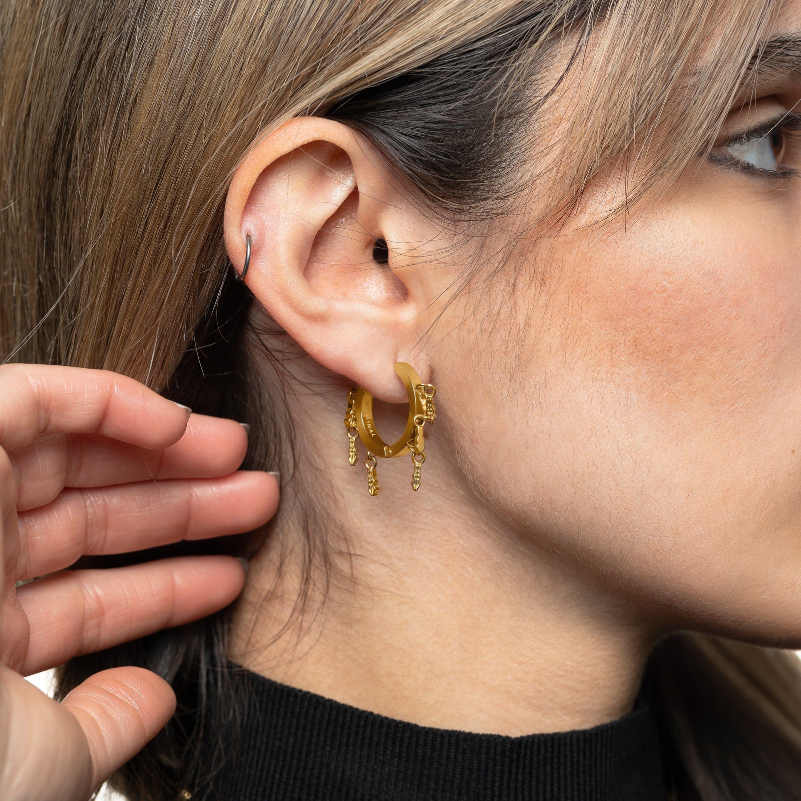 Model moves their hair away to show the gold Raining Tatreez Hoop Earrings on their right ear.