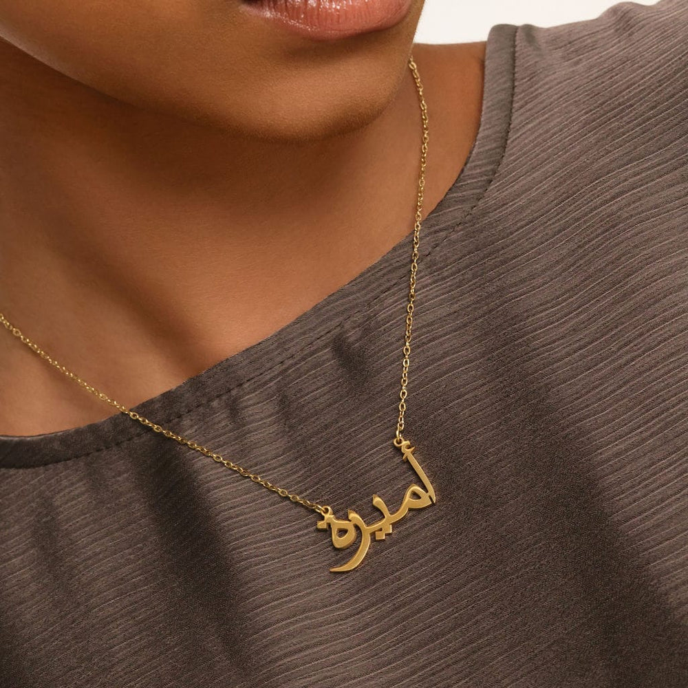 Close up of the Ready Name Necklace against the brown textured fabric of the model's clothing.