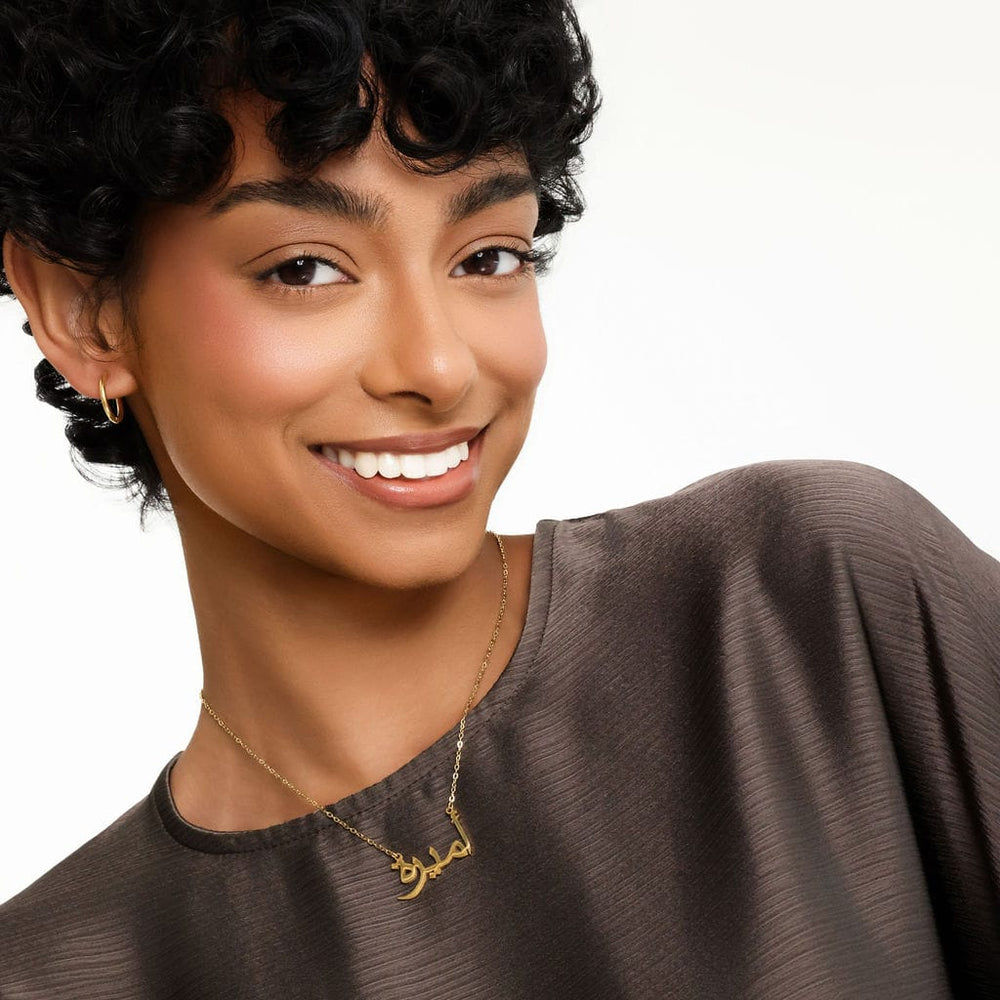 Photo of the model smiling to the camera. The model is wearing the gold Ready Name Necklace