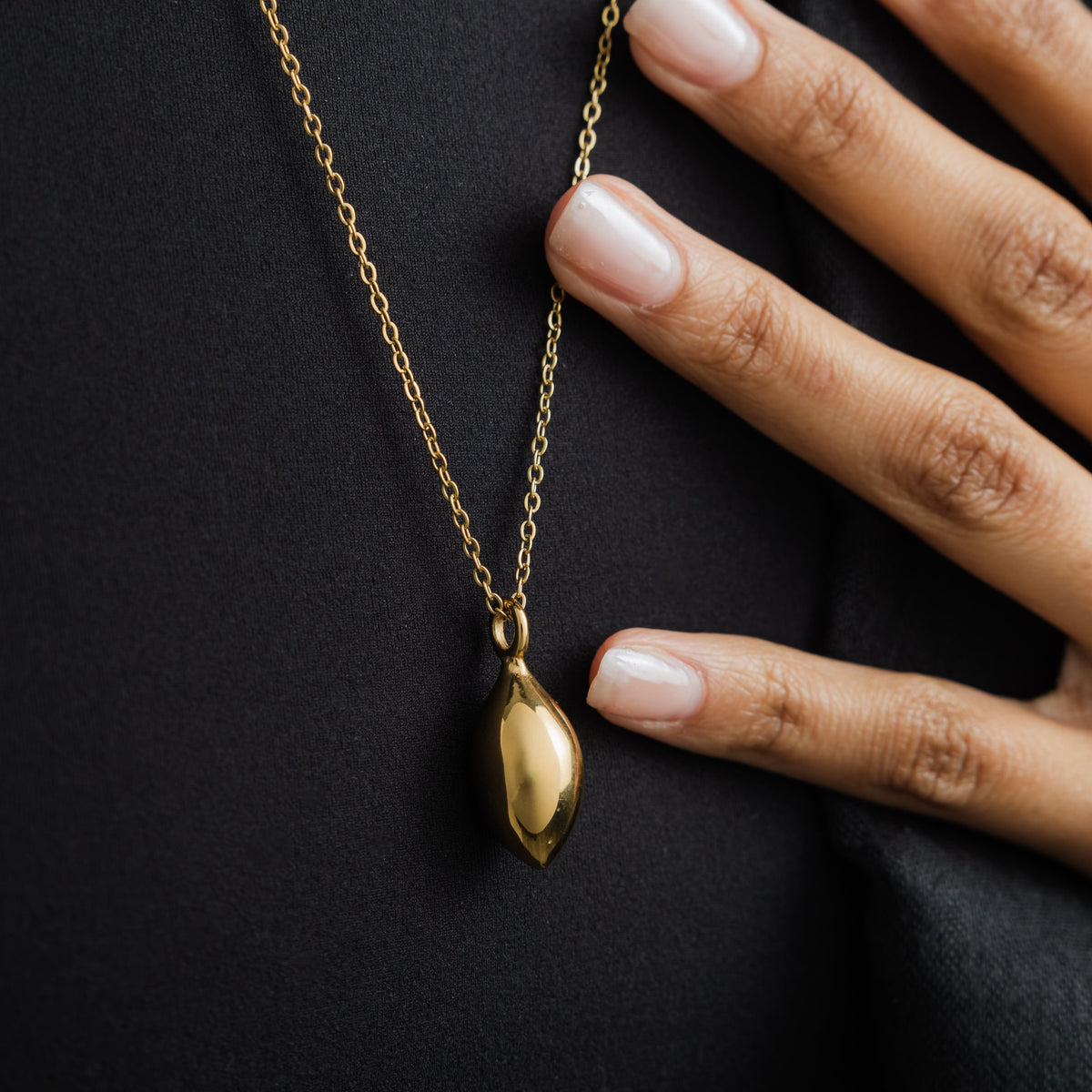 Close up of the gold Palestinian Olive Necklace against the black fabric of the model's clothing.