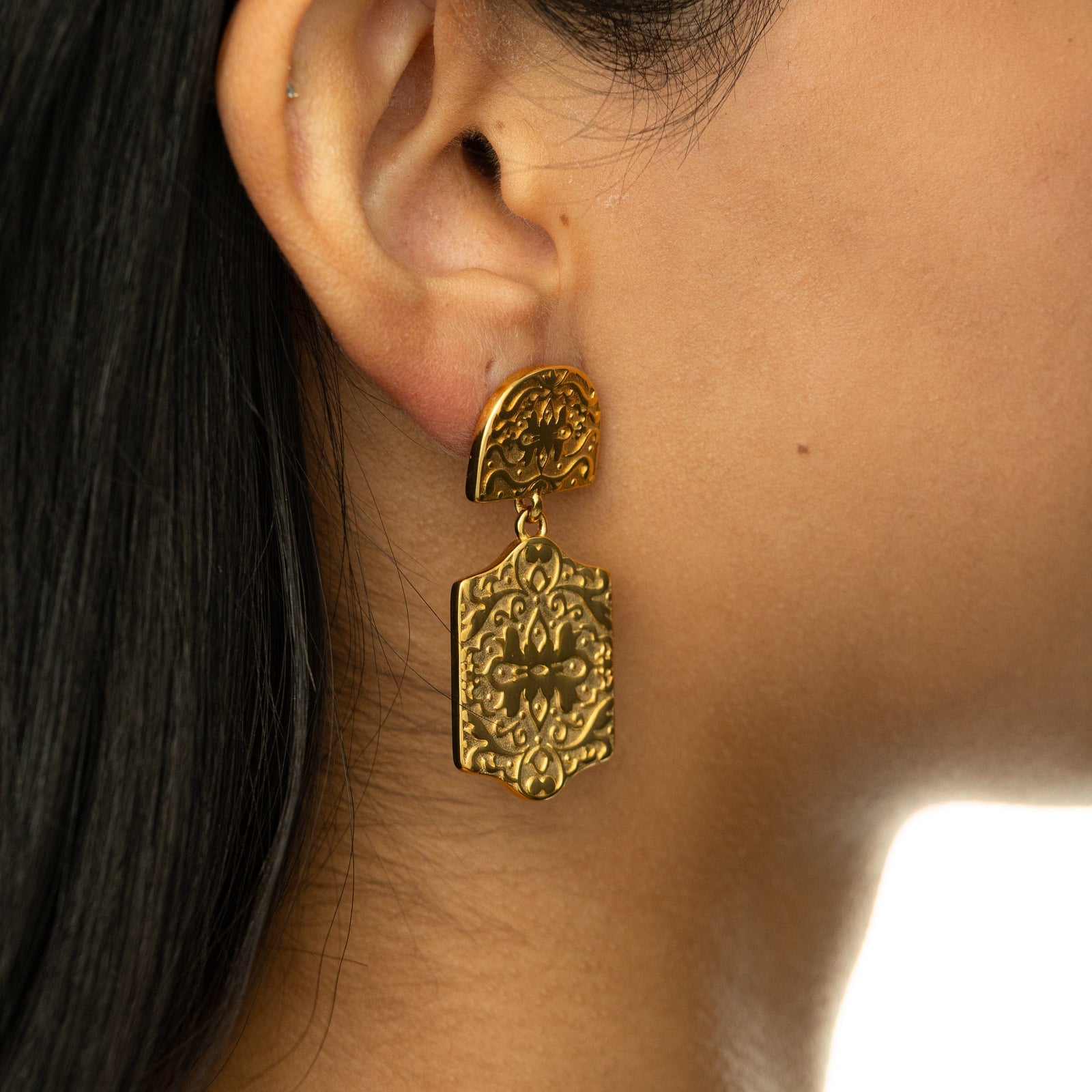 Gold Roaming Earring worn on ear, showing detailed engraved floral and vine design on the two-part drop structure.