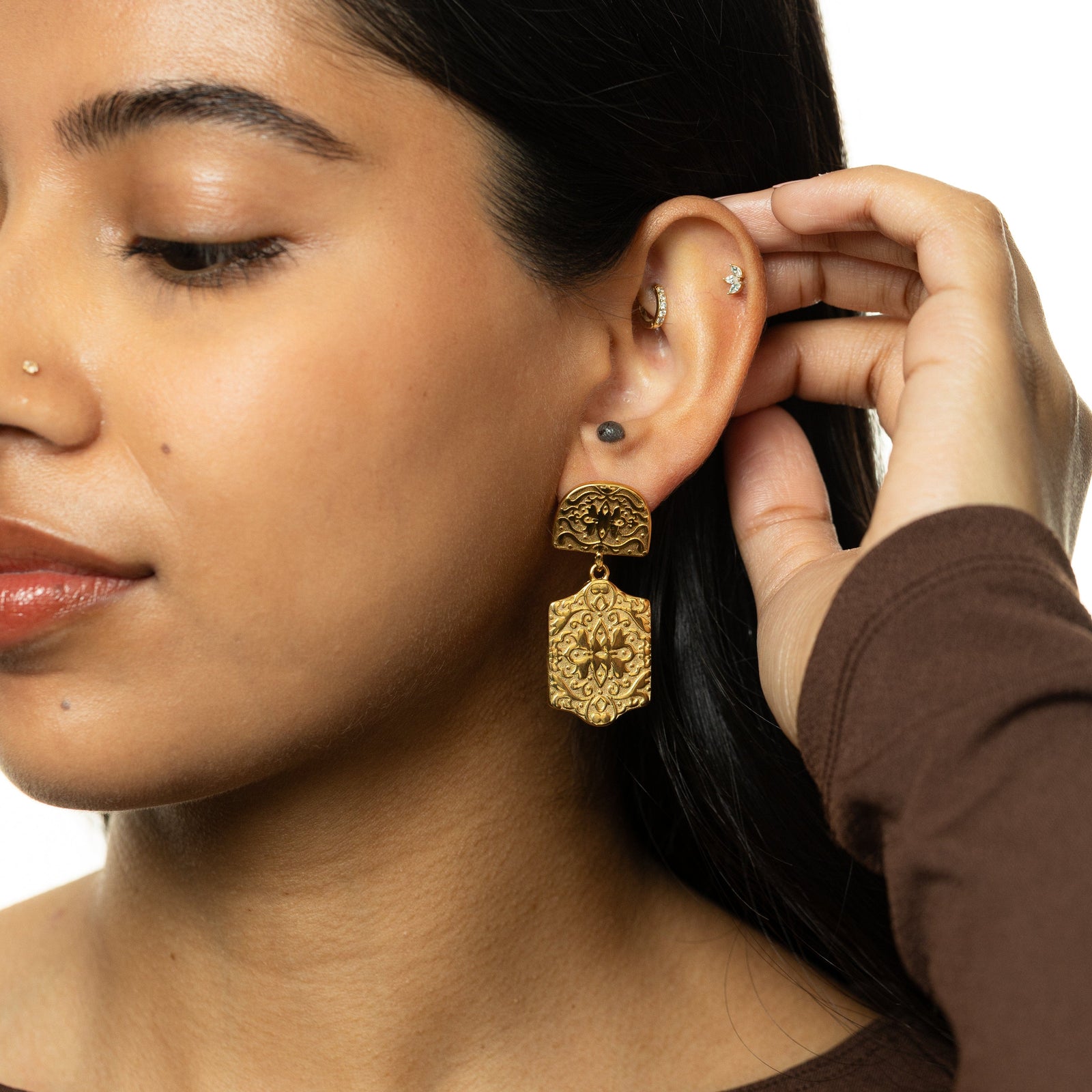 Gold Roaming Earring with engraved floral details dangling from ear, hand resting near hair.