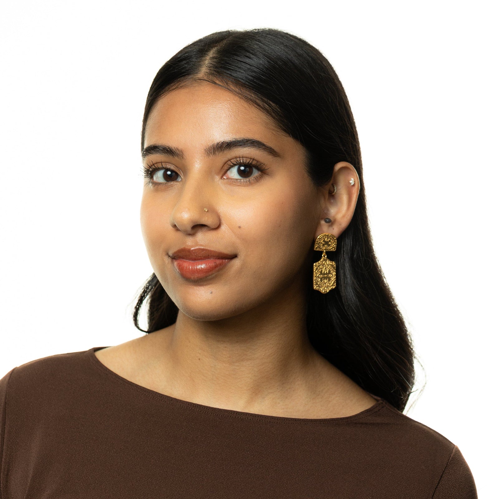 Woman wearing gold Roaming Earrings with engraved patterns, styled with brown top.