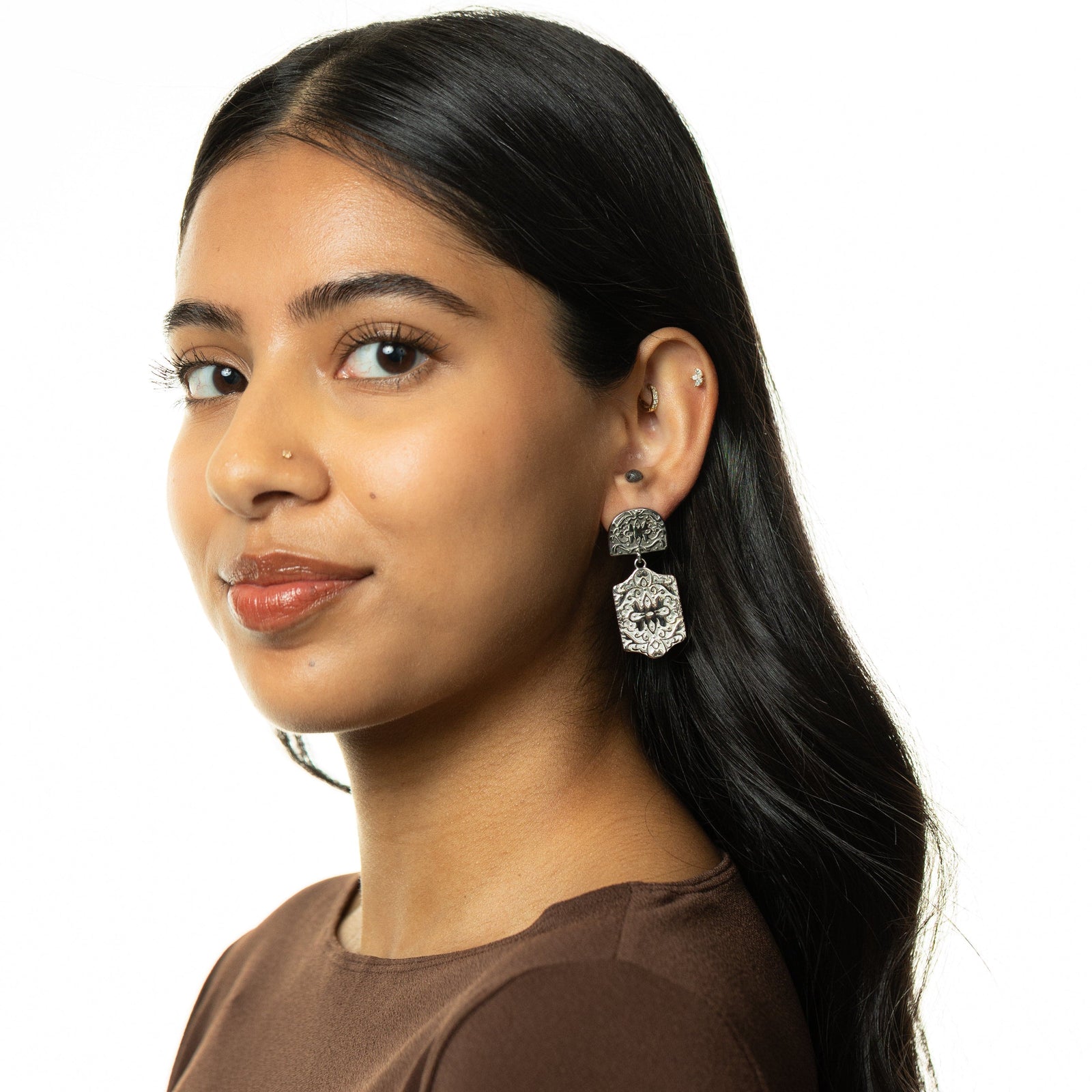 Woman wearing silver Roaming Earrings with engraved floral designs, styled with brown top.