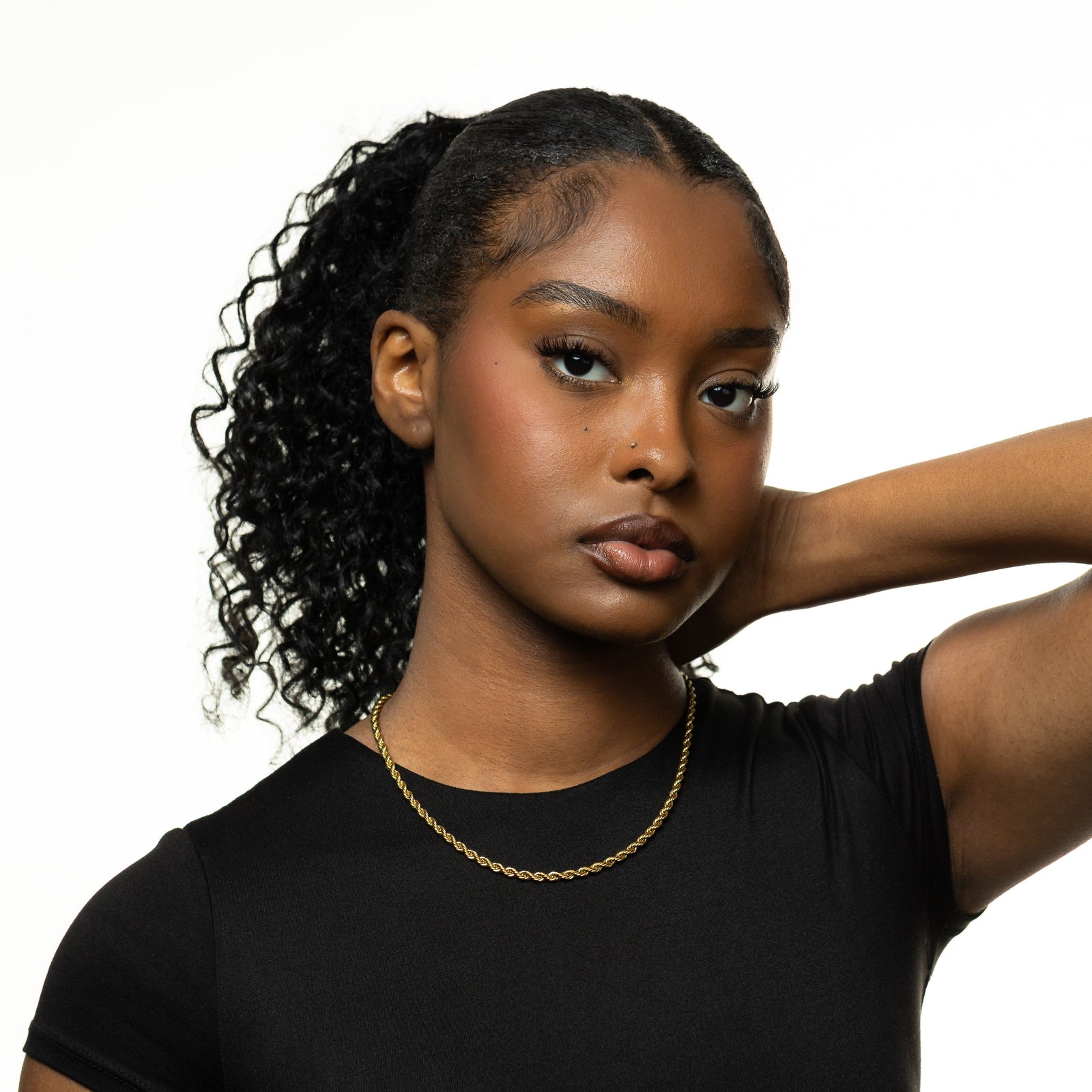 Photo of the model looking at the camera with their hand at the back of their neck. The model is wearing the gold Rope Chain Necklace.