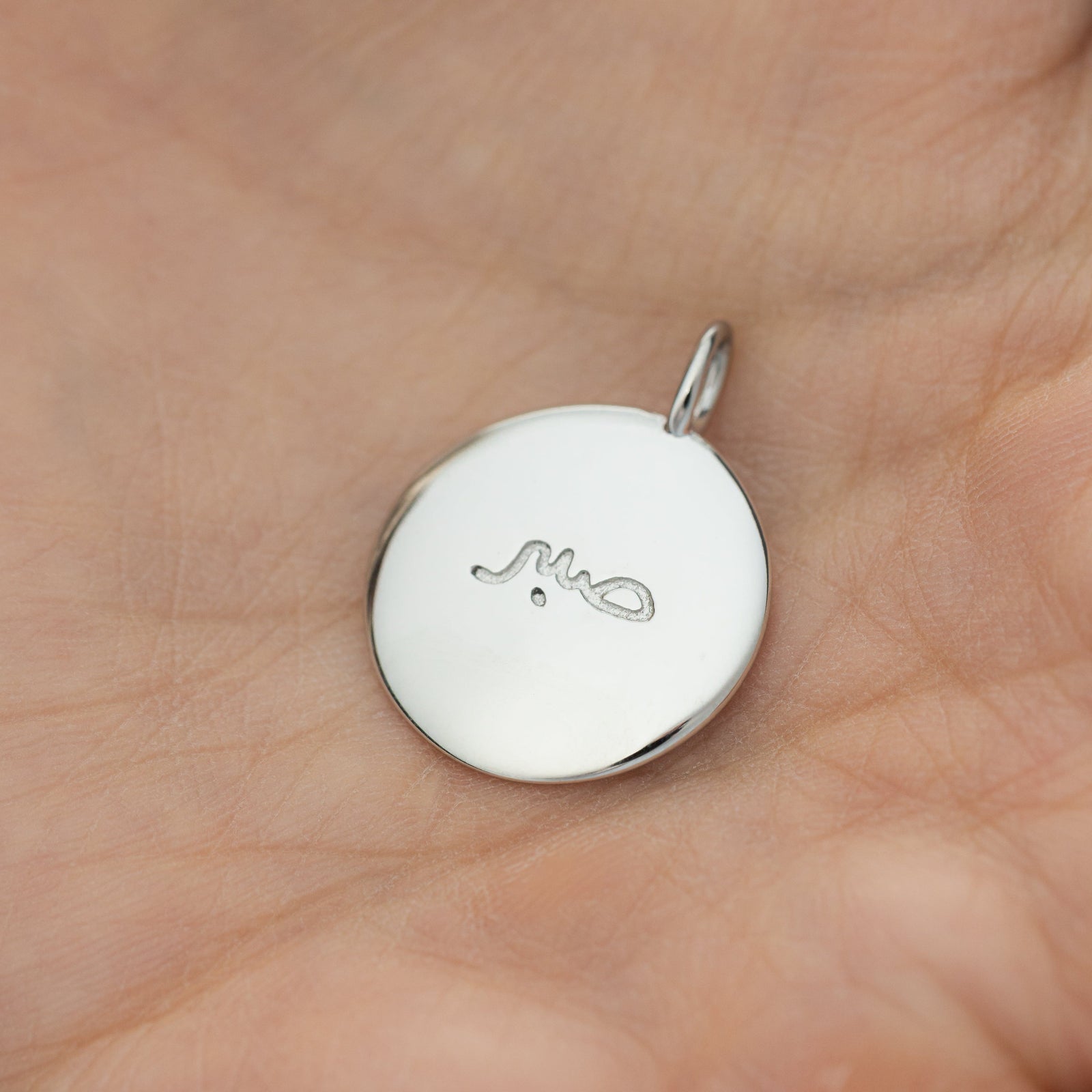 Silver Sabr charm placed gently in an open palm, showing the engraved Arabic calligraphy close-up.