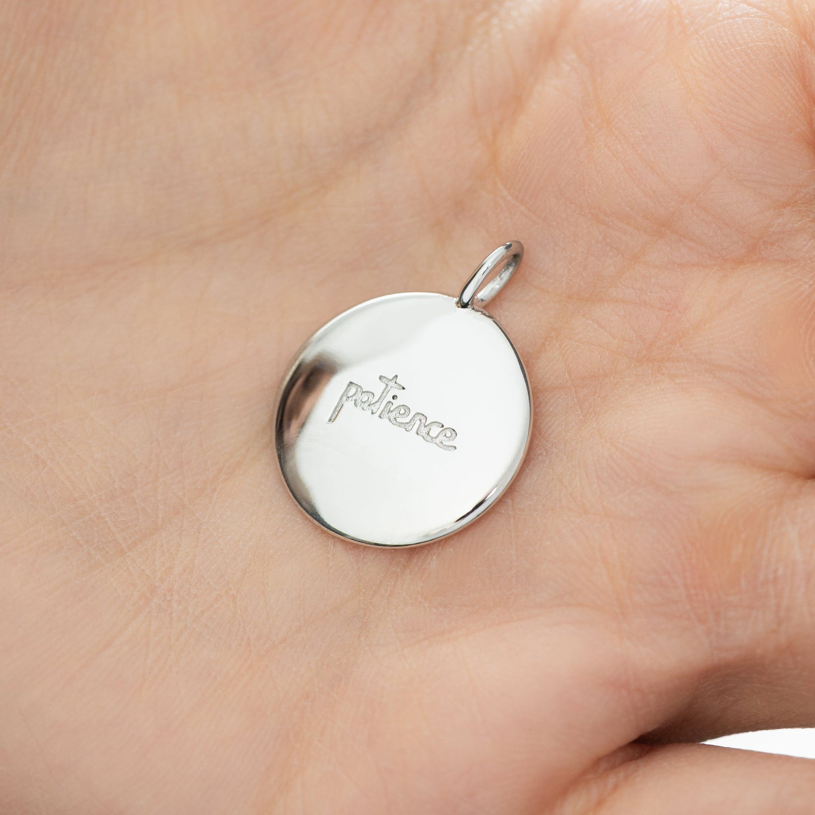 Silver Sabr charm with Arabic engraving, resting on hand to highlight the size.