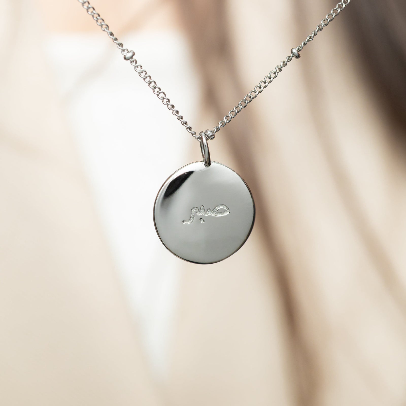 Silver beaded necklace featuring the silver "Sabr" charm hanging from the chain.