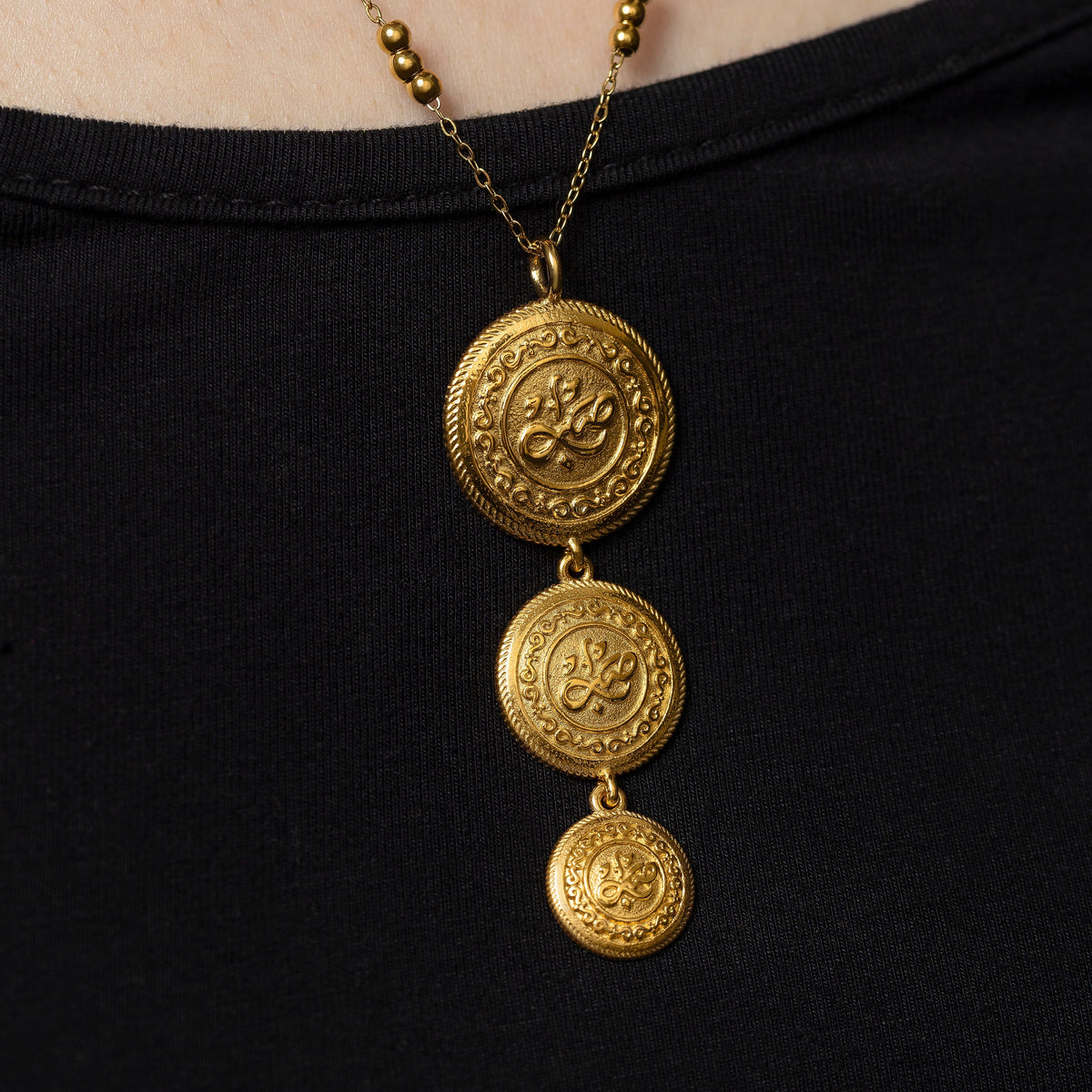 Close up of the three gold coin necklace on a black background