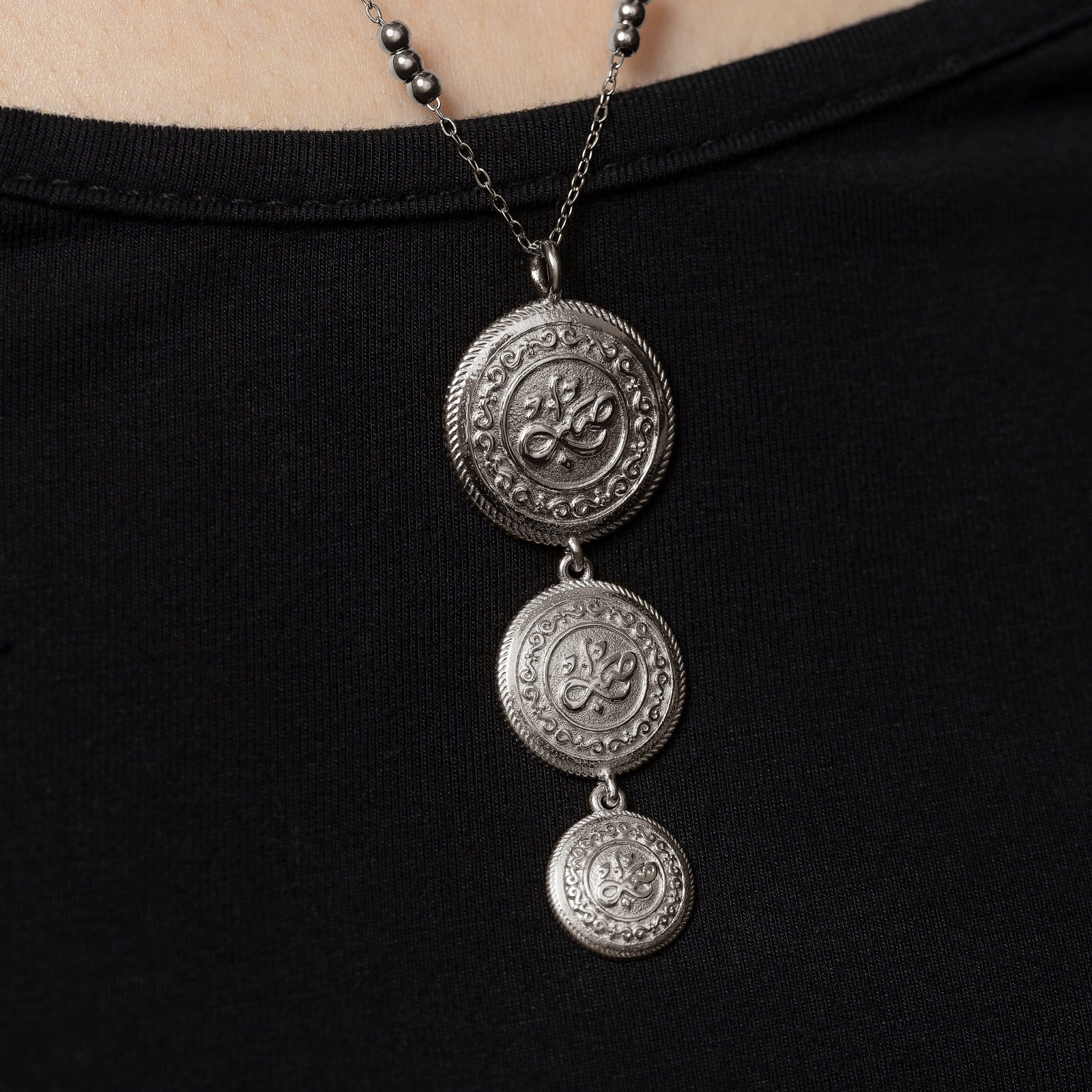 Close up of the three silver coin necklace on a black background