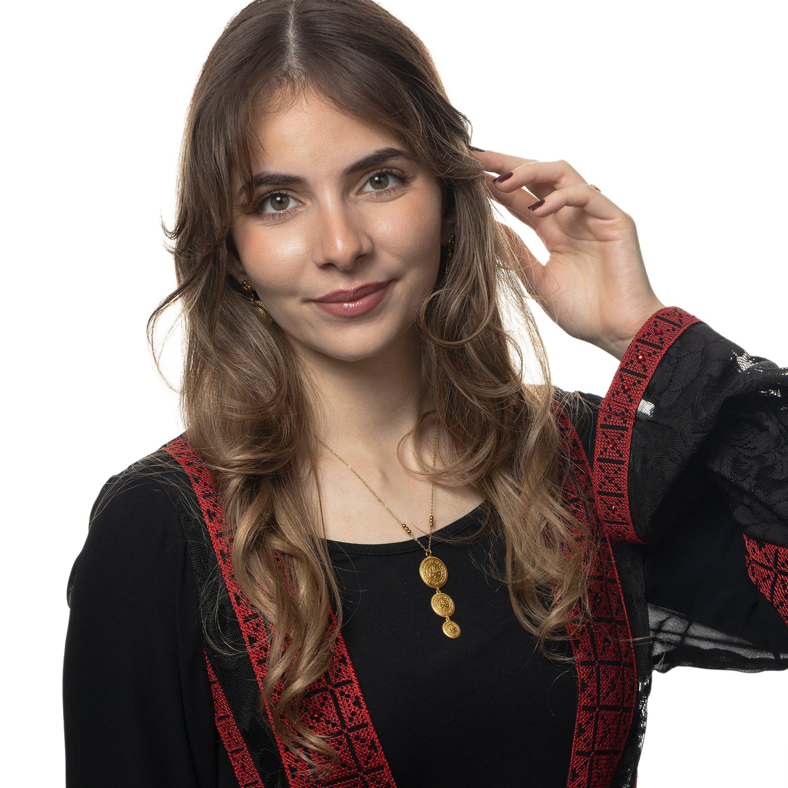 Photo of the model smiling to the camera while touching their hair with their left hand. The model is wearing the gold Sabr | Patience Coin Necklace