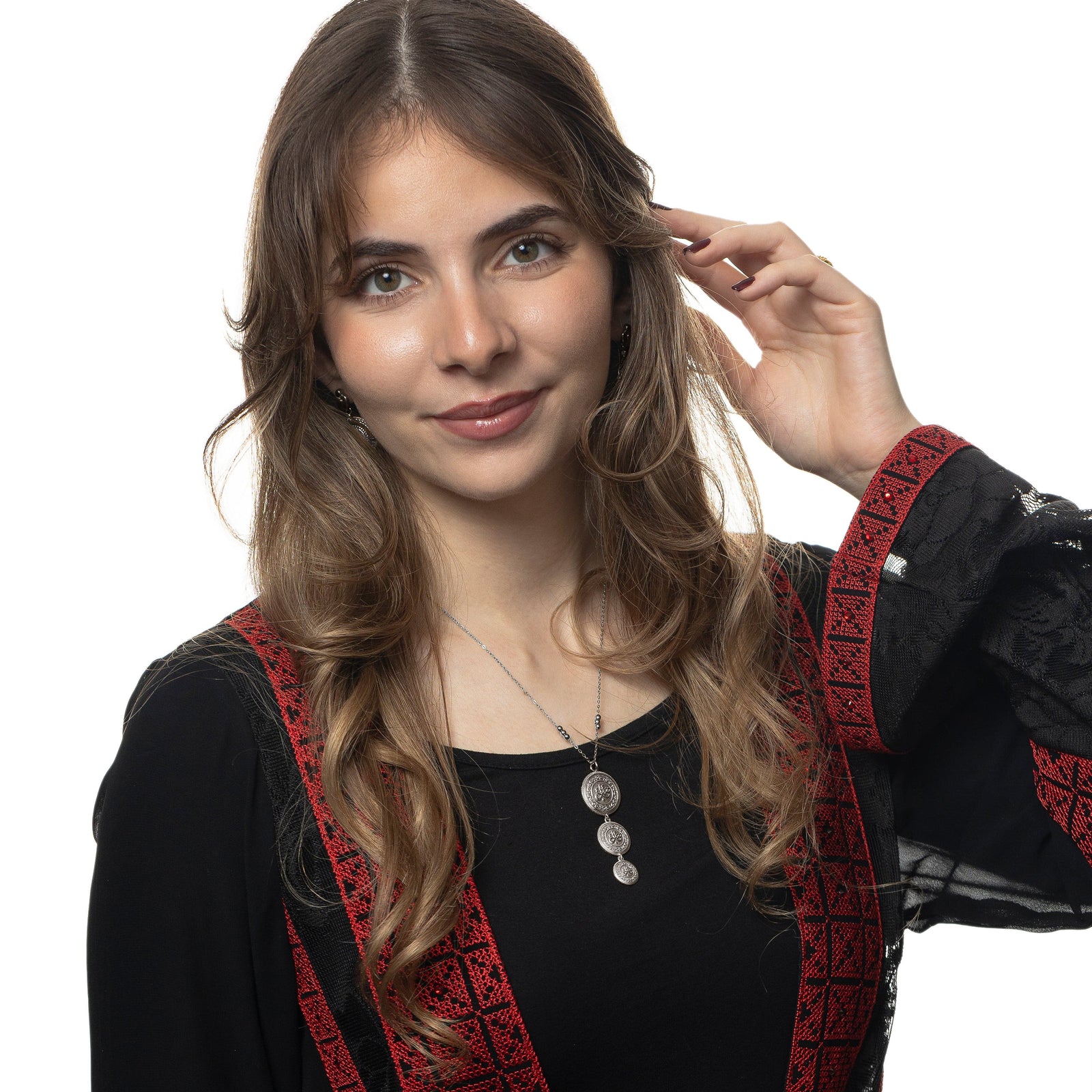 Photo of the model smiling to the camera while touching their hair with their left hand. The model is wearing the silver Sabr | Patience Coin Necklace