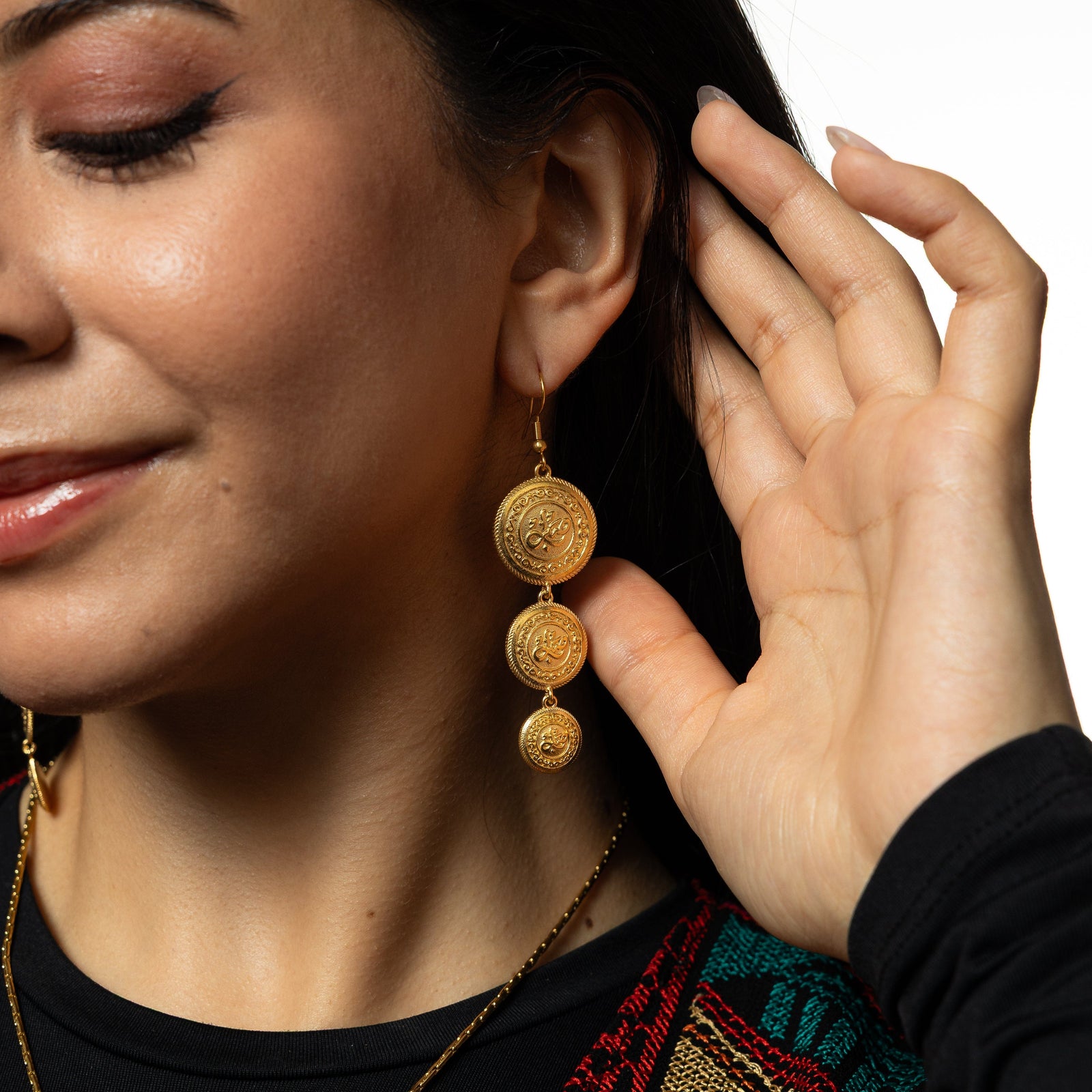 Model holds their hair away from their left ear showing the dangling gold Sabr | Patience Coin Earrings.