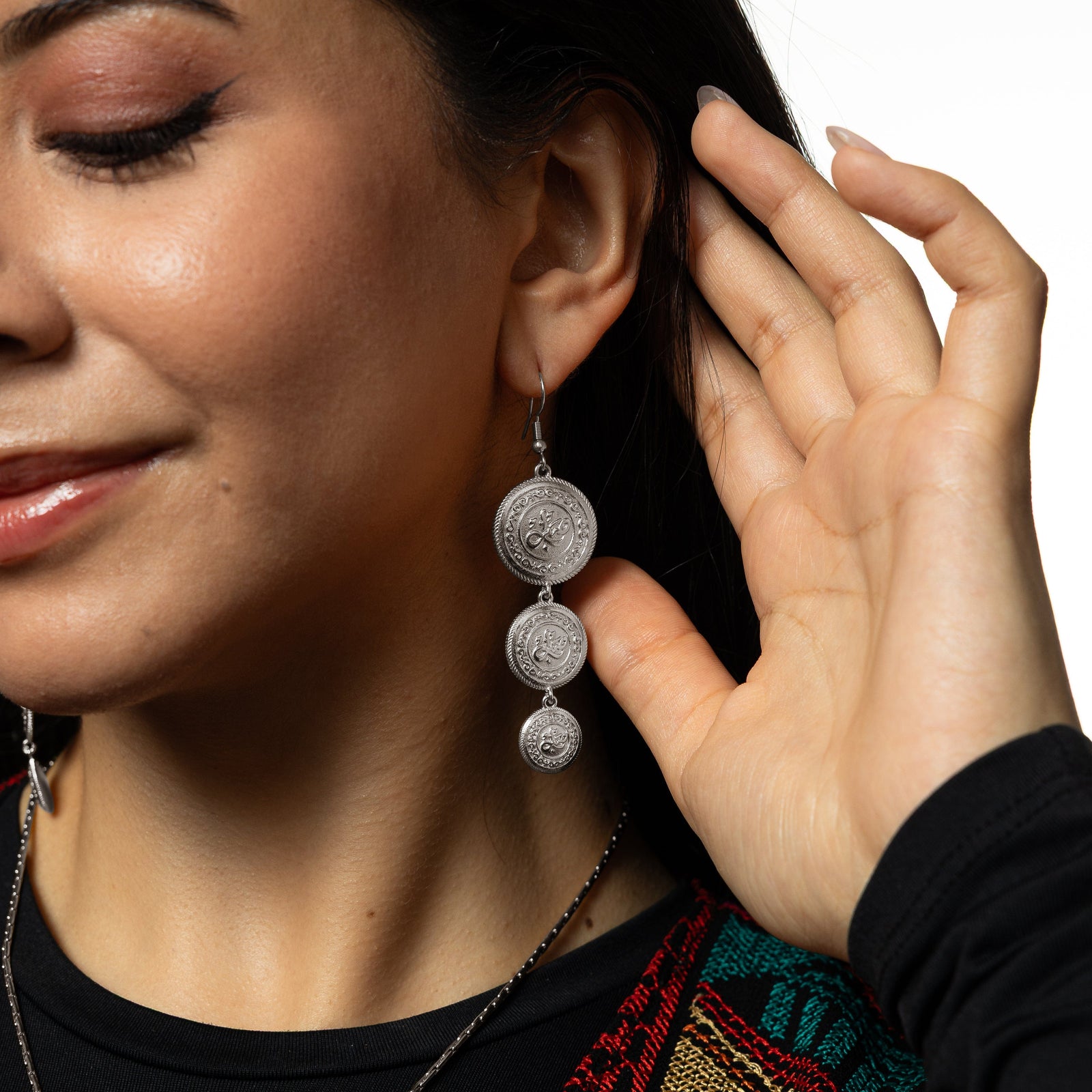 Model holds their hair away from their left ear showing the dangling silver Sabr | Patience Coin Earrings.