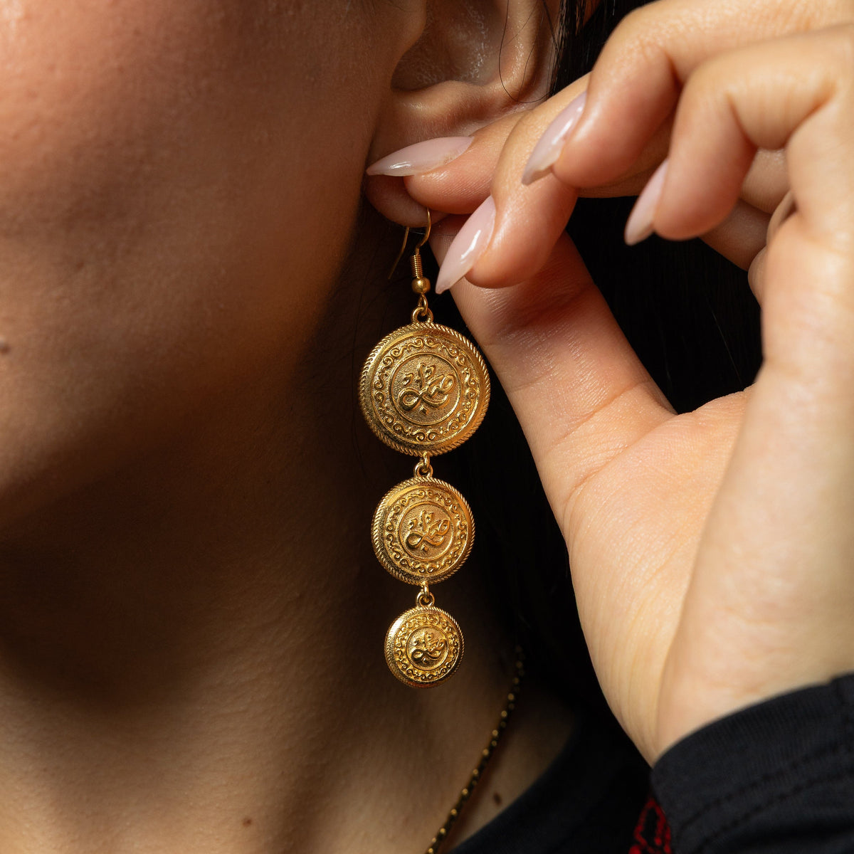 Gold Sabr | Patience Coin Earring dangling as the model holds their left ear.