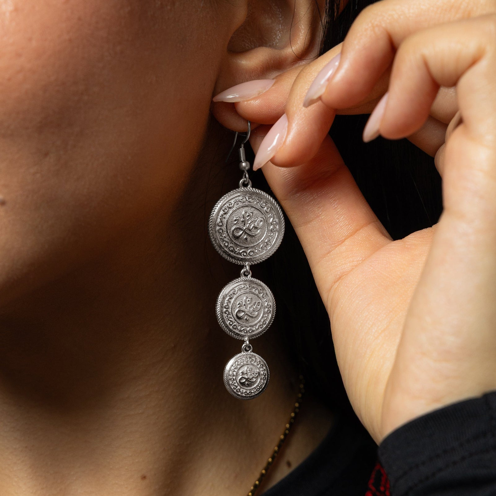 Silver Sabr | Patience Coin Earring dangling as the model holds their left ear.