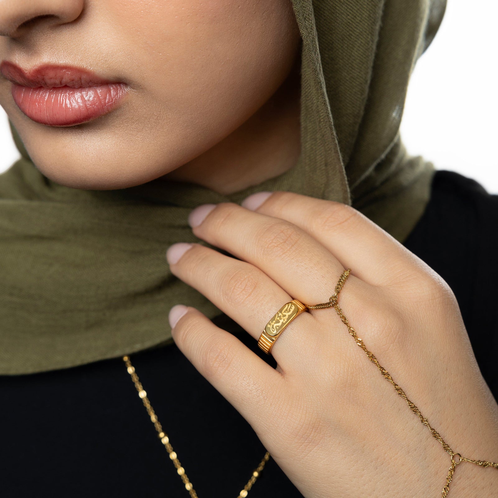 Gold Sakinah serenity ring paired with gold twistedchain bracelet, worn on hand resting near chin.