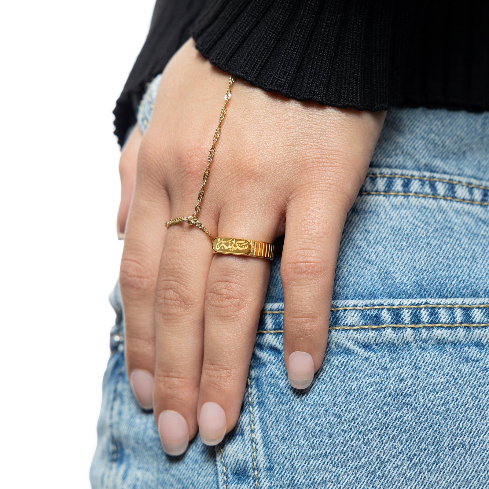 Gold Sakinah serenity ring and twisted hand chain worn on hand resting on light-wash denim.