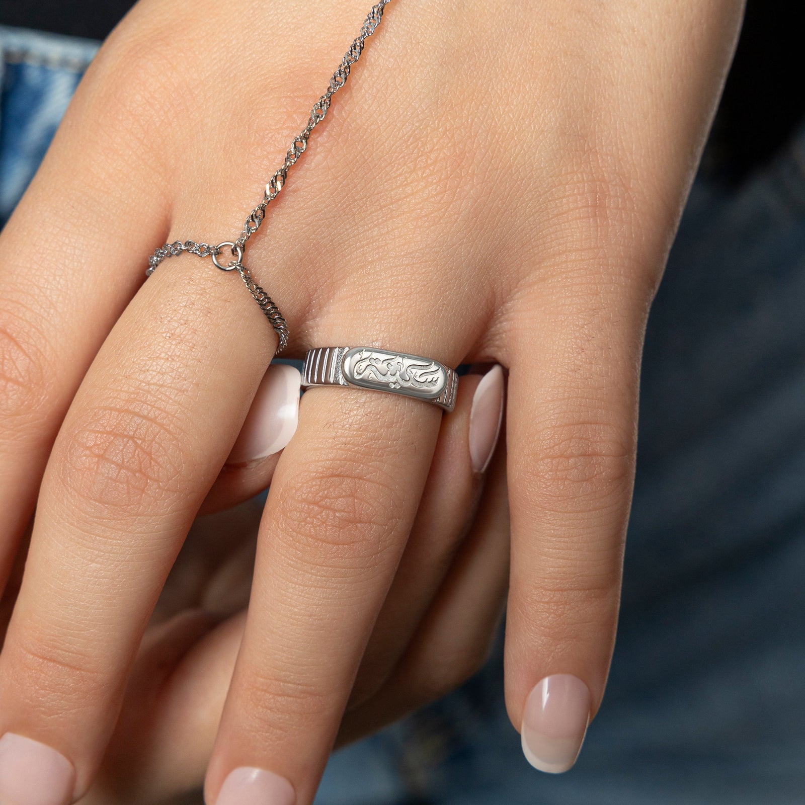 Woman's hand with Silver Sakinah serenity ring with engraved Arabic calligraphy and silver twisted hand chain.