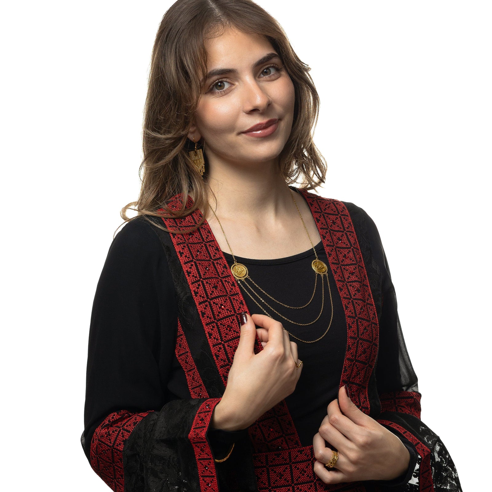 Photo of the model smiling at the camera. The model is wearing the gold Salam | Peace Layered Token Necklace, a pair of gold dangling earrings, and a gold ring on their left ring finger.