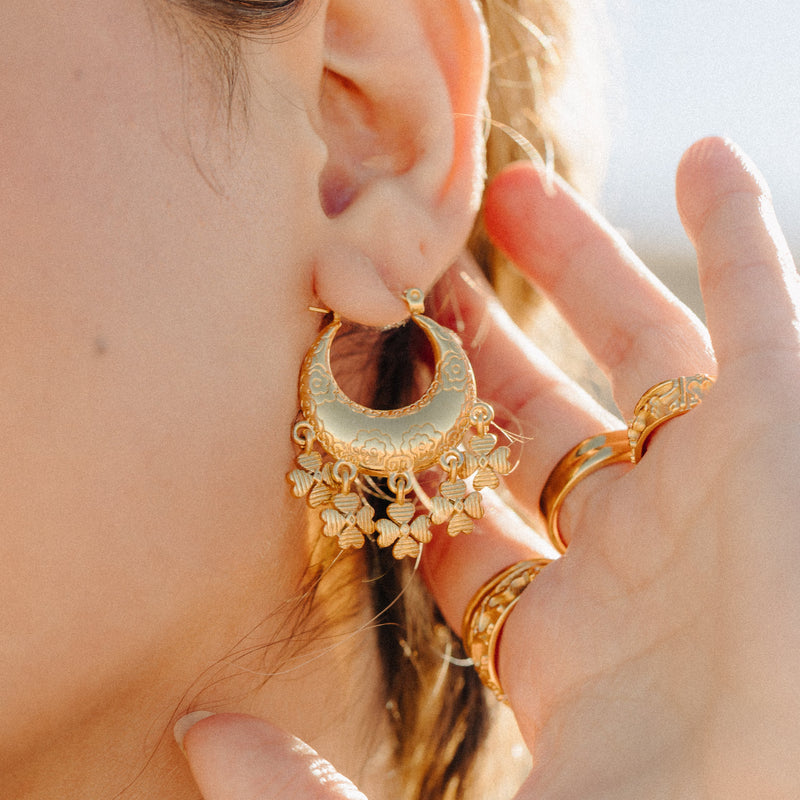 Gold Levantine Garden Hoop Earring with floral etched details and dangling charms worn on a woman’s ear.