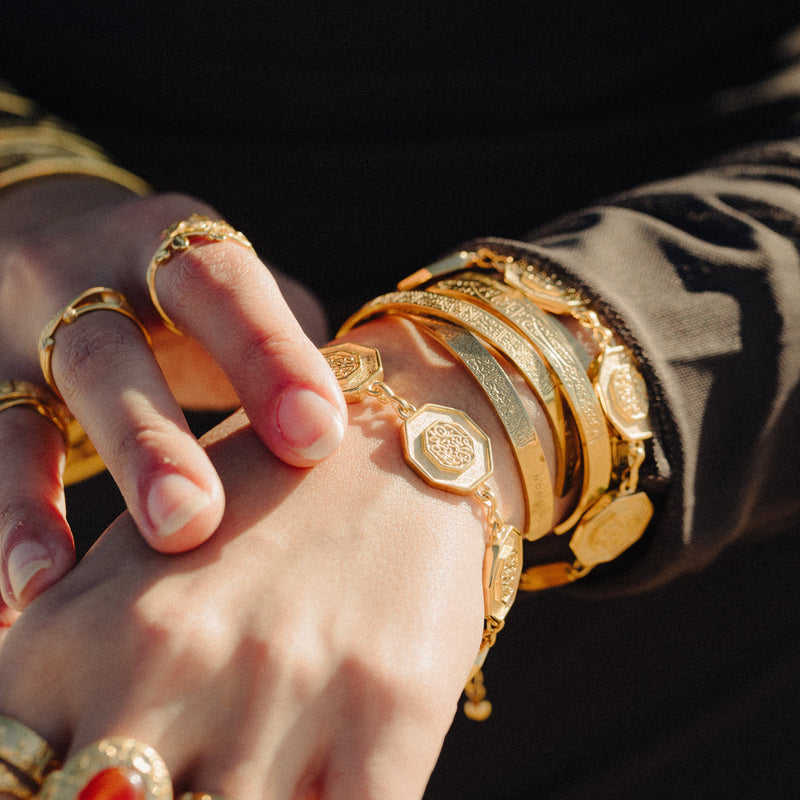 “Our Roots Run Deep” Dotted Bracelet in gold styled with multiple gold bangles and rings.