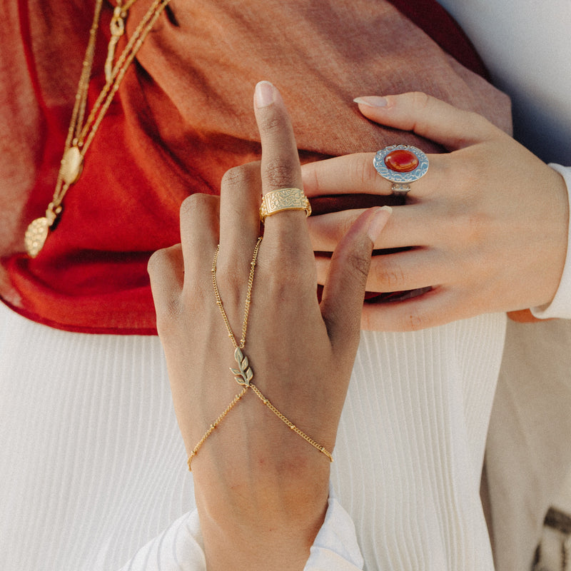 Gold Palestinian Olive Branch Hand Chain styled with layered jewelry and rings.