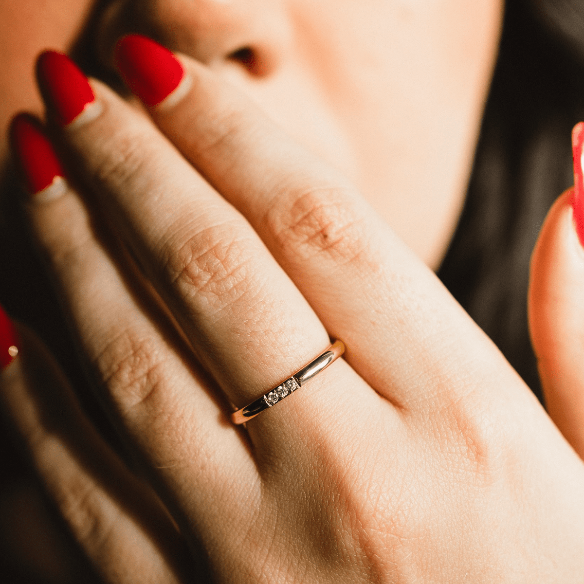 Woman wearing a thin gold ring with three bezel-set stones on her finger.