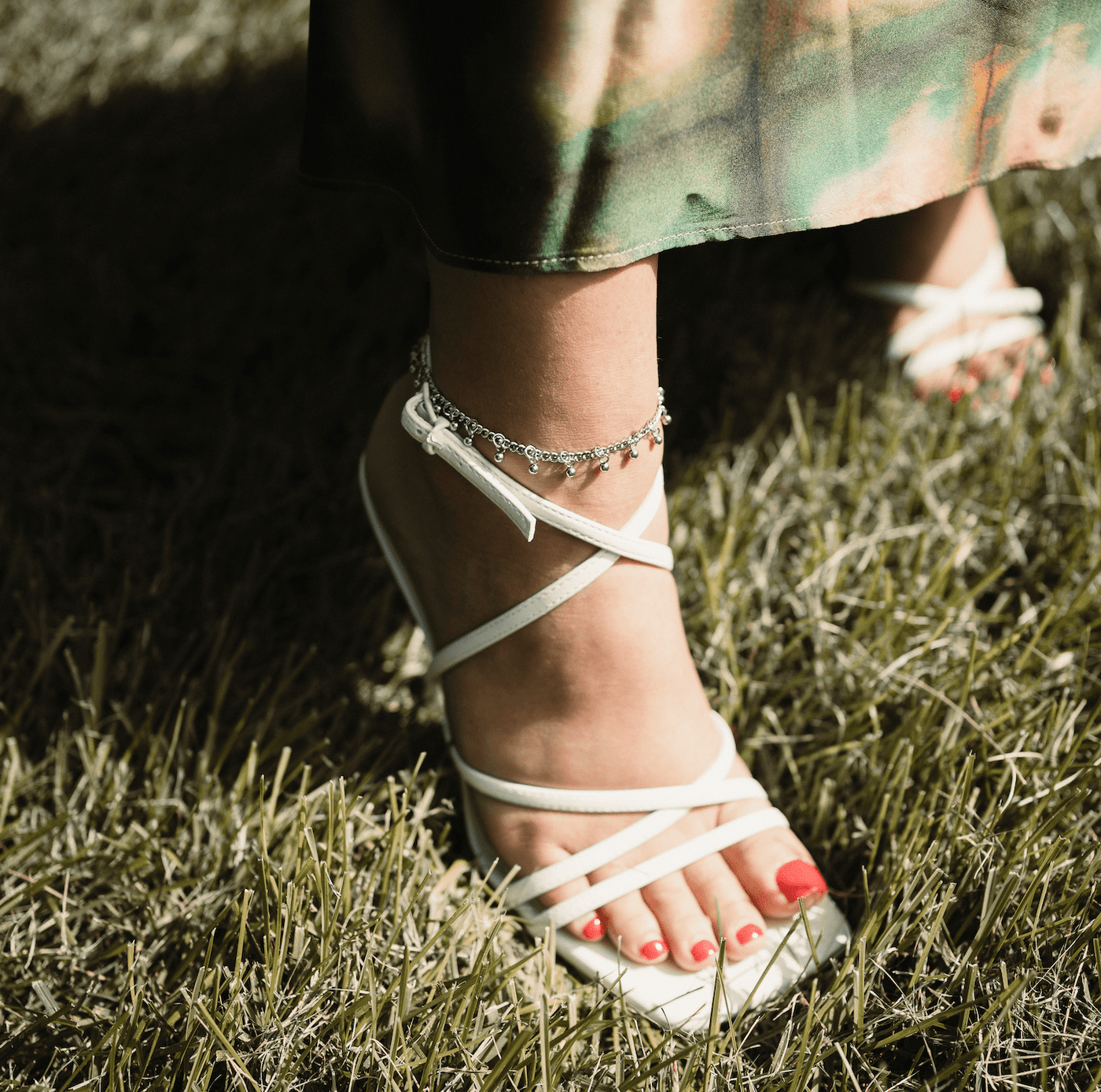 A model showcasing the silver Dangling Dotted Anklet. The anklet encircles her ankle, emphasizing the subtle dangling charms against a neutral-toned background.