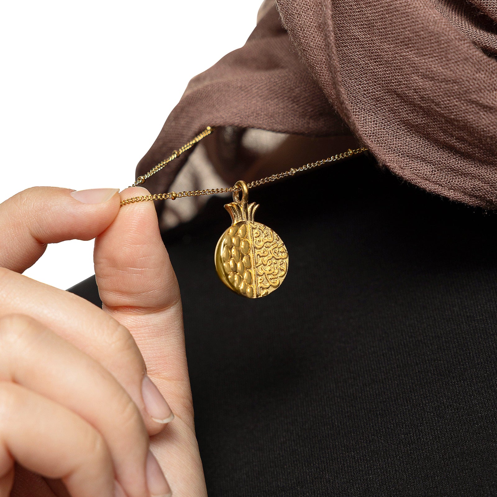 Model holding the gold Seeds of Gratitude Necklace pendant, showing the detailed pomegranate design.