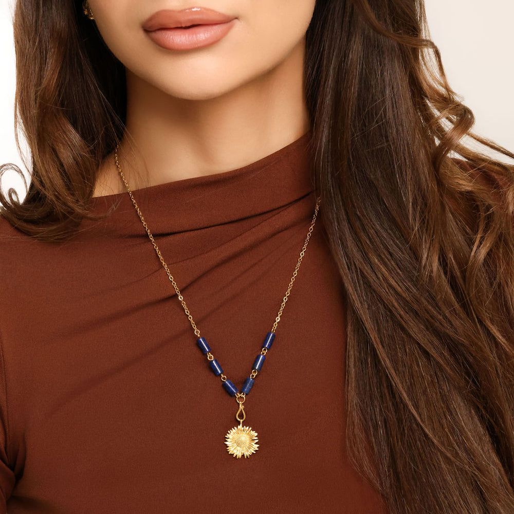 Woman wearing an 18k gold plated necklace with a detailed sunflower pendant and deep blue tube beads.