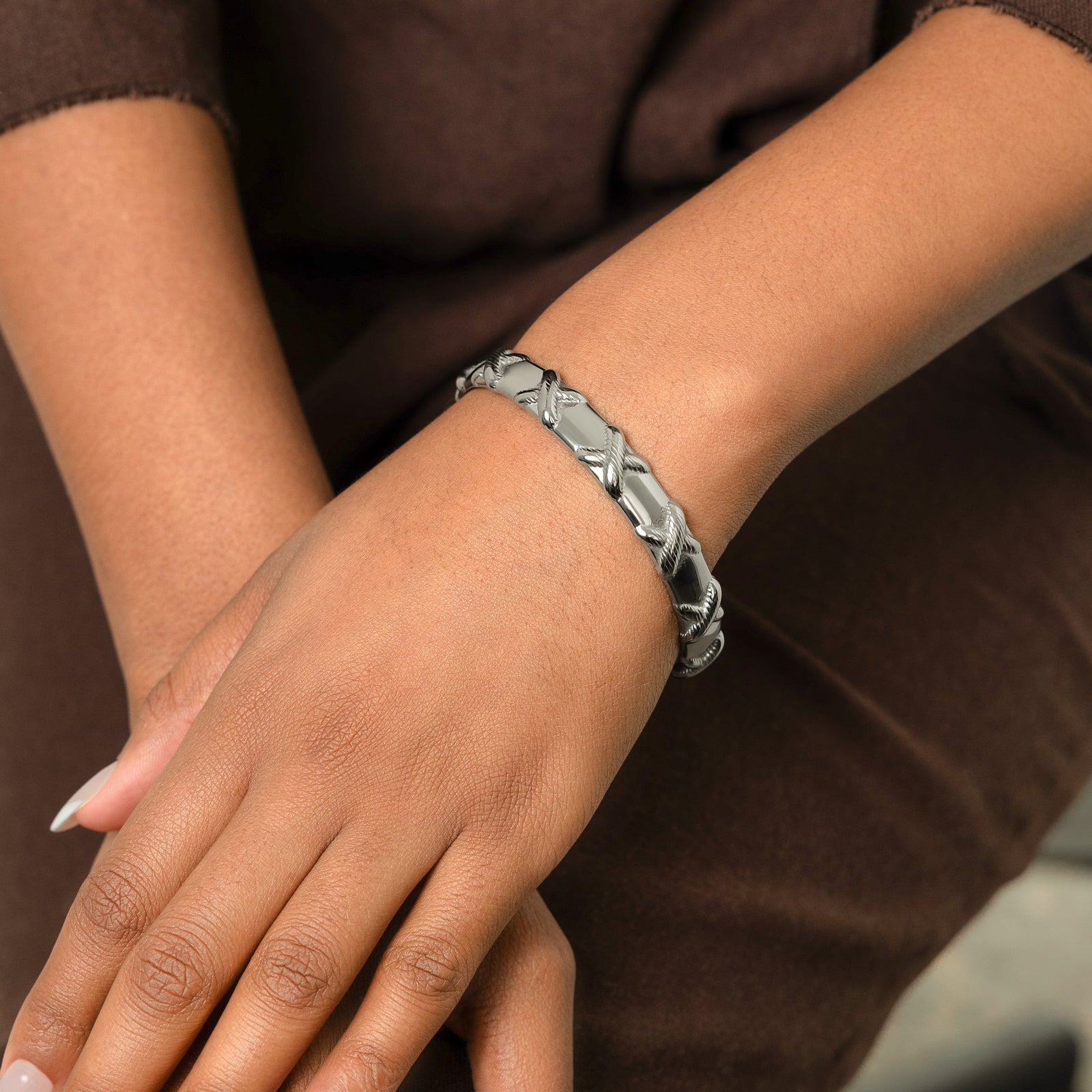 Photo of the model's hands on their lap. The model is wearing the silver "Leave Your Mark | X" Bangle on their left wrist.