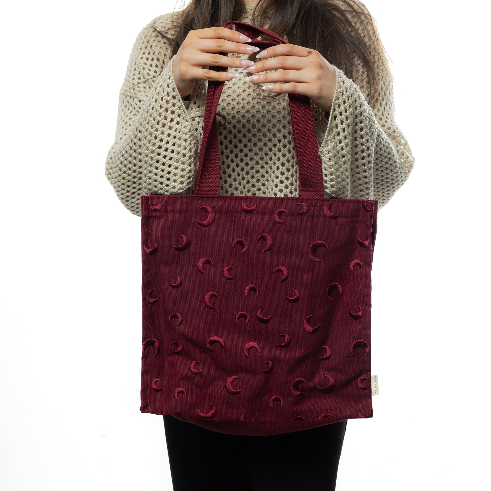 Woman holding the Skyfall Tote Bag in front of her torso with both hands. The crescent moon details are evenly spaced across the bag’s front.